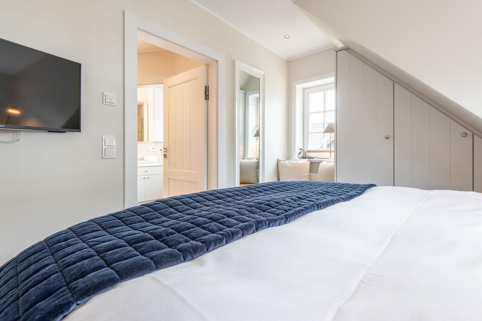 Schlafzimmer mit Bett, TV und Blick in Bad und Schlafbereich.