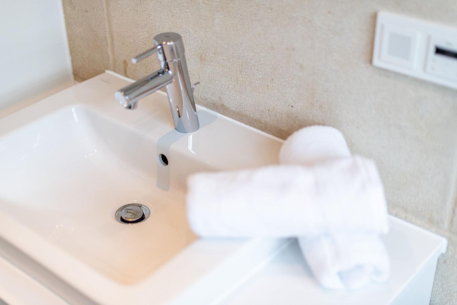 Waschbecken mit silbernem Wasserhahn und weißer Handtuchrolle