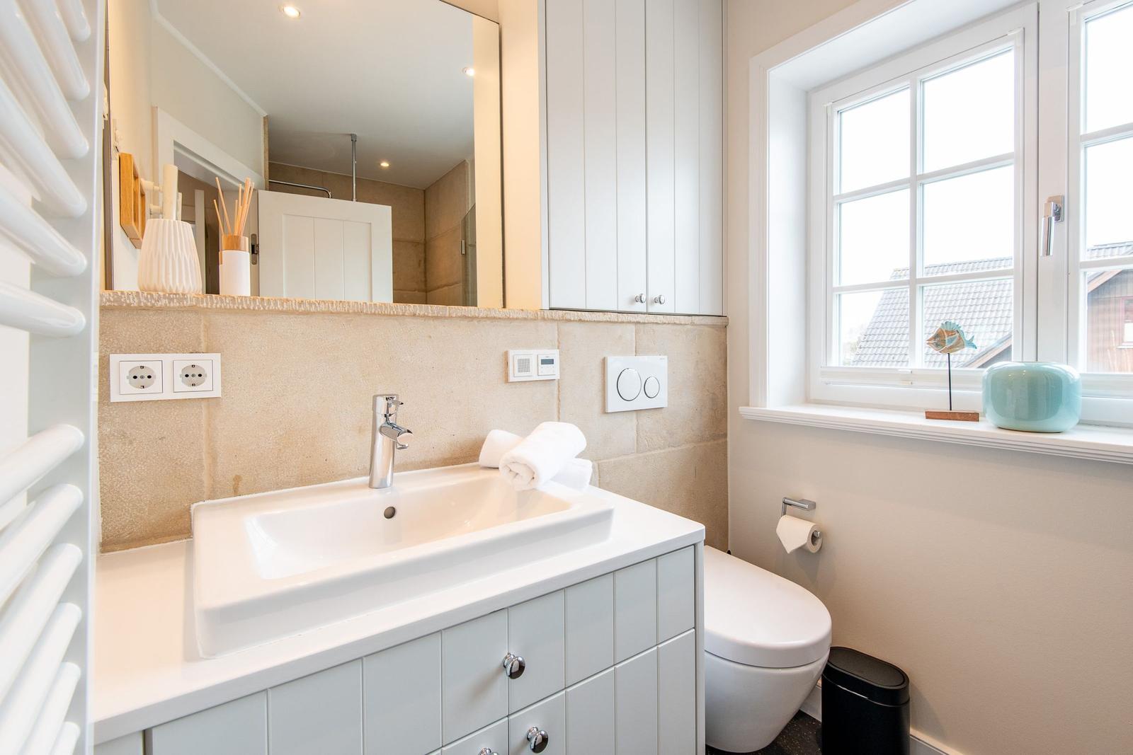 Badezimmer mit Waschbecken, Spiegel, Toilette und Fenster.