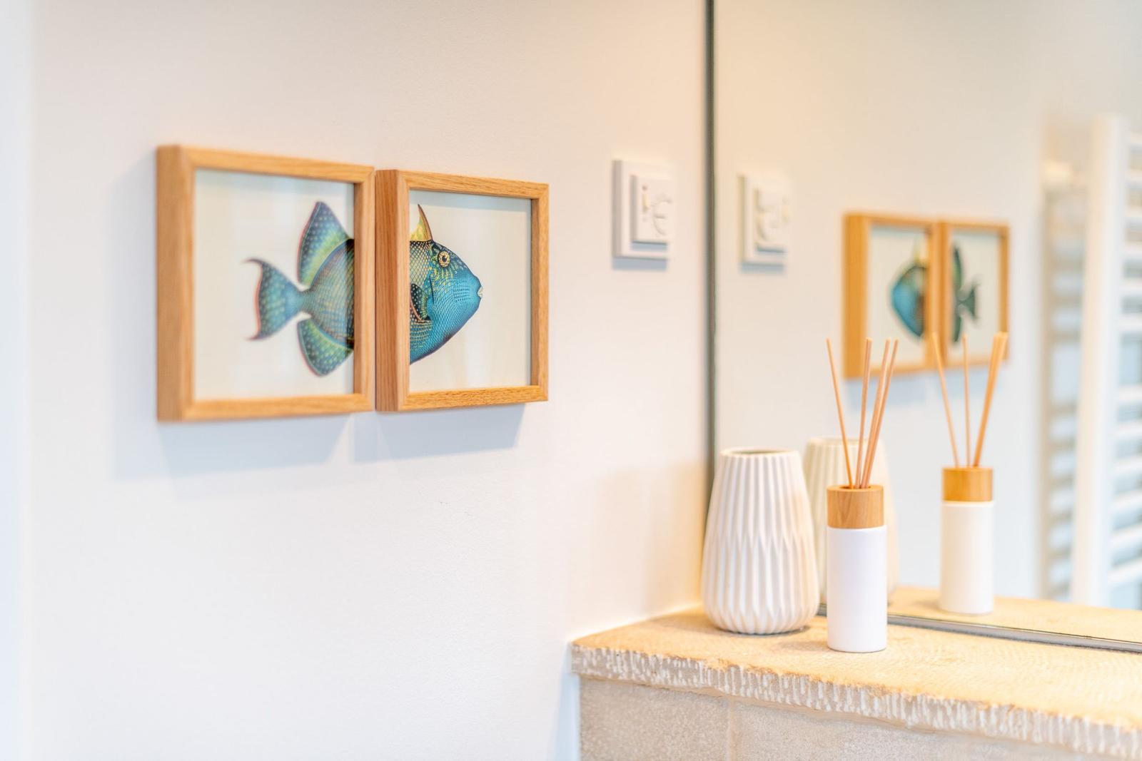 Zwei Bilder mit Fischen hängen an der Wand neben einem Spiegel mit Aromalampe.
