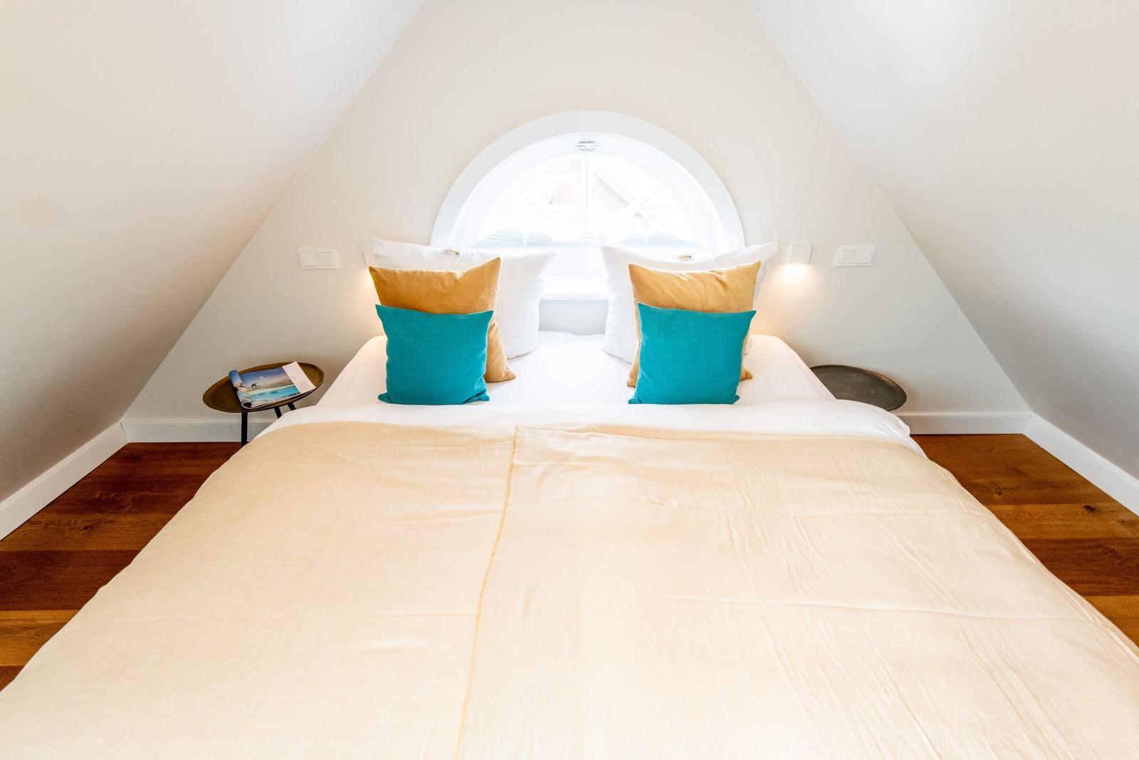 Schlafzimmer mit Dachschrägen, Bett mit Kissen und runden Nachttischen.