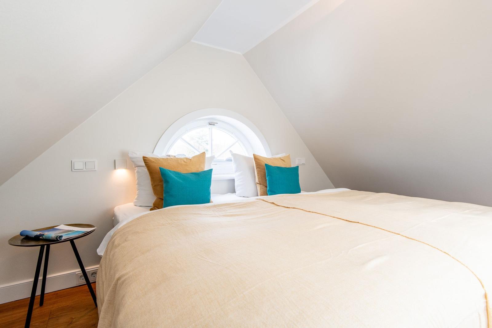 Schlafzimmer mit Dachschrägen, runden Fenster und Bett mit Kissen.