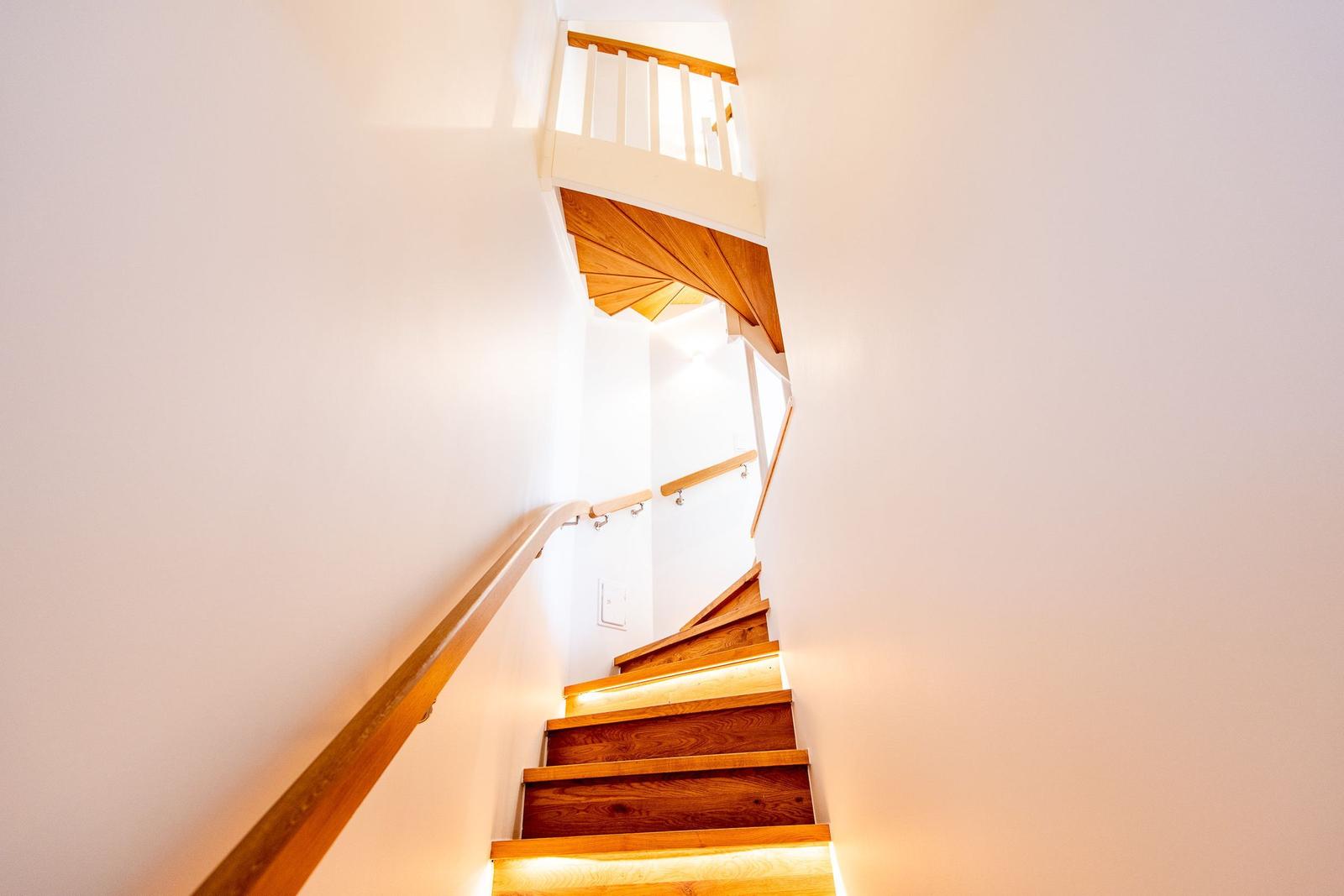 Holzgetreppe mit beleuchteten Stufen und Geländer führt nach oben.