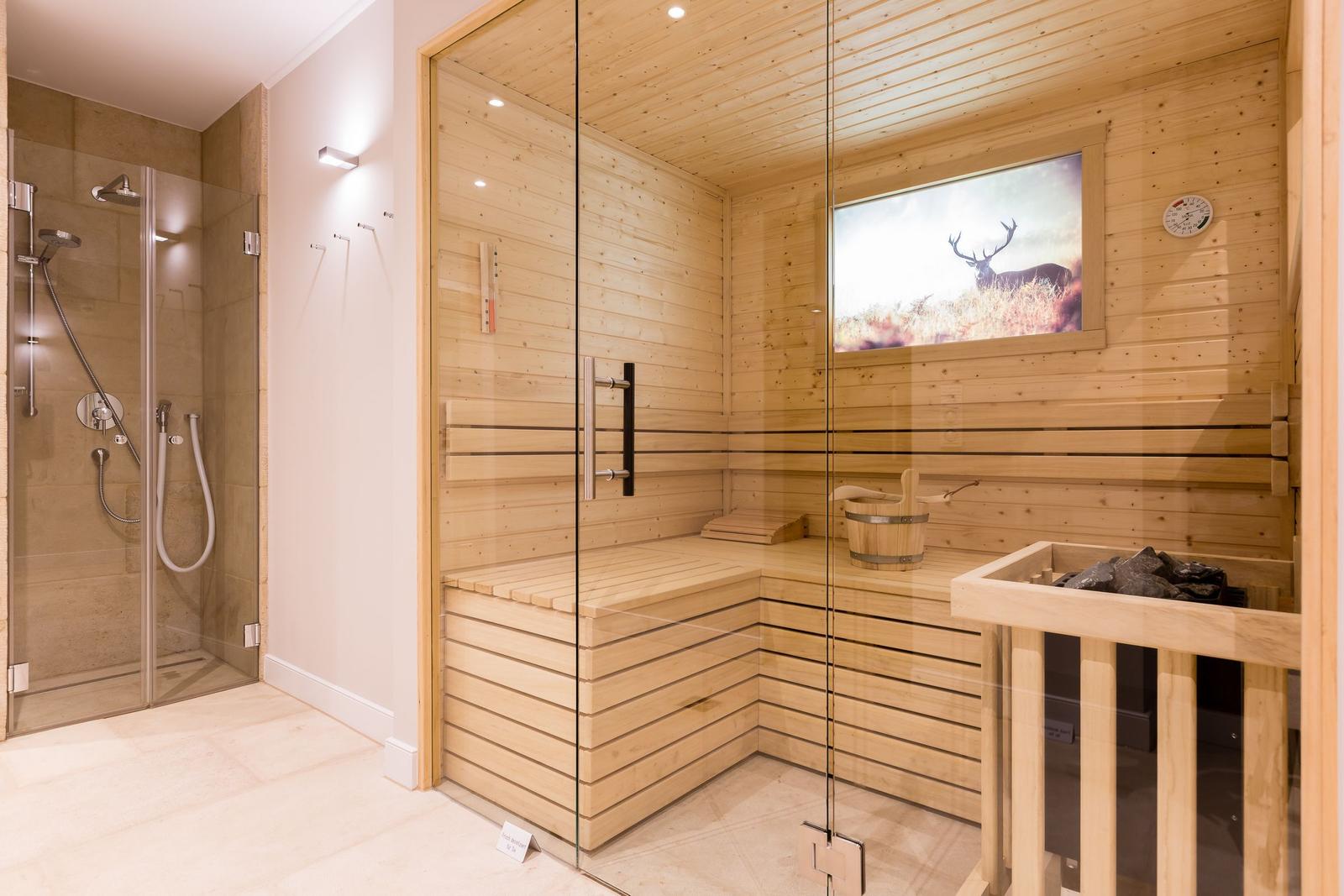 Sauna mit Holzbank und Glaswand. Dampfdusche daneben. Wandbild mit Hirsch.