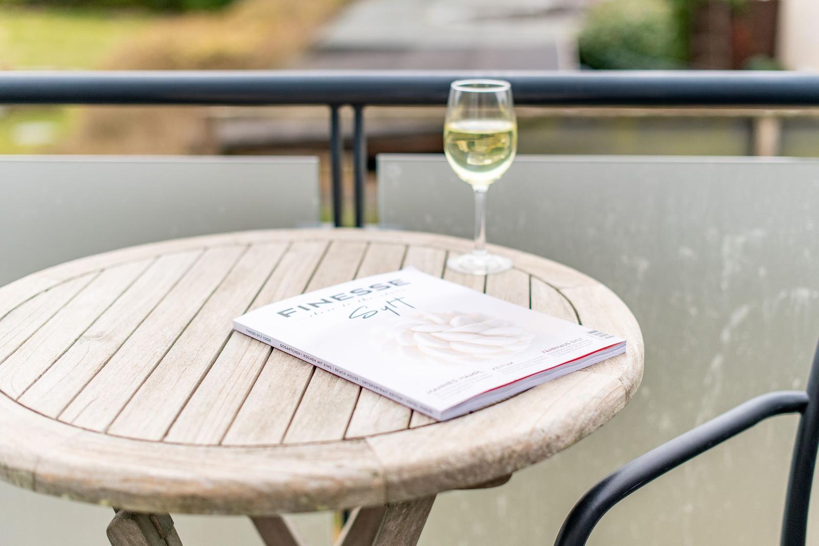 Runder Holztisch auf Balkon mit Glas Weißwein und Magazin.