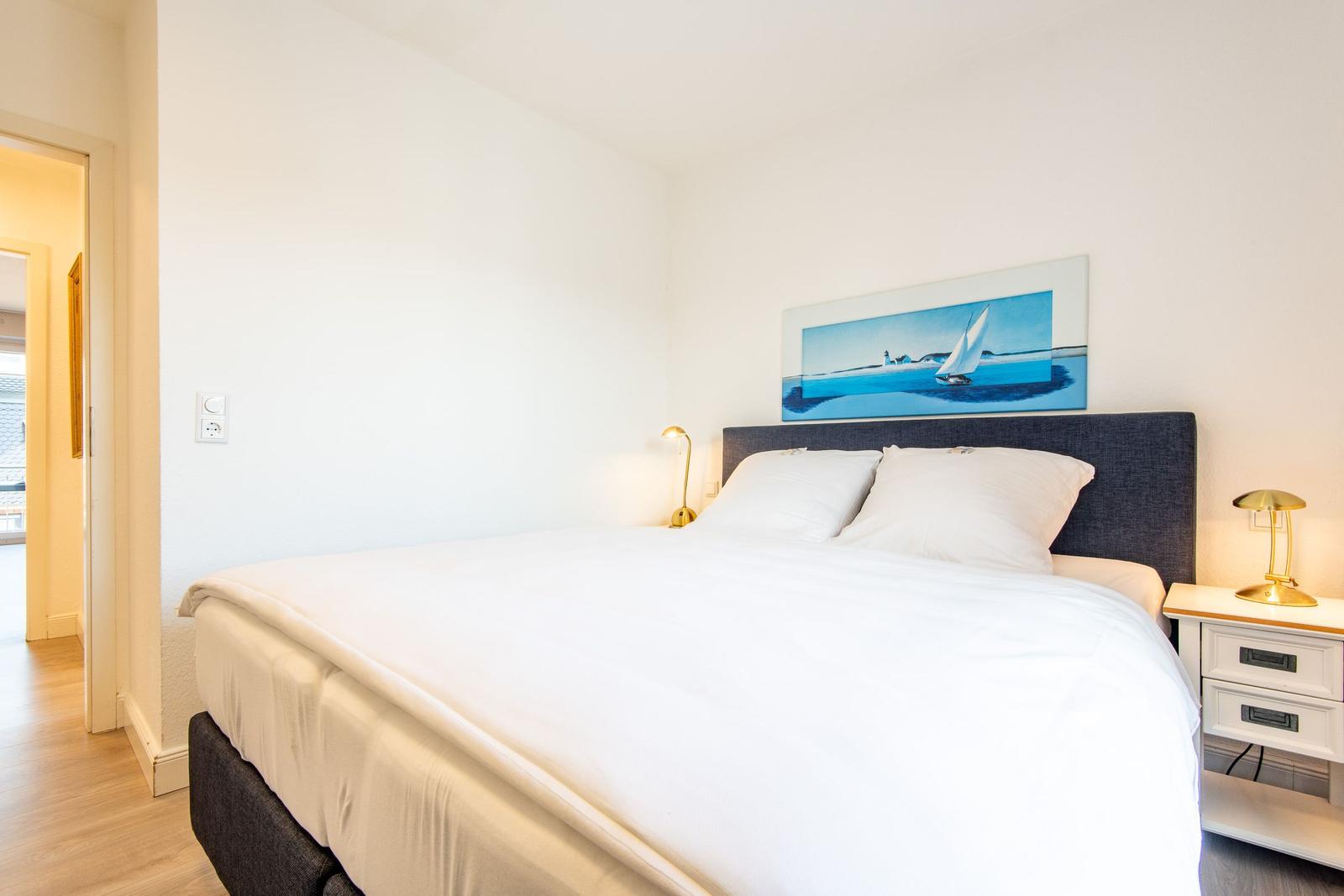 Schlafzimmer mit Bett, Nachttisch und Wandbild mit Segelboot.