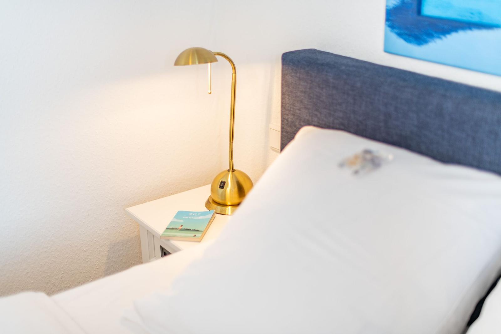 Schlafzimmer mit Bett, Nachttisch und goldener Lampe.