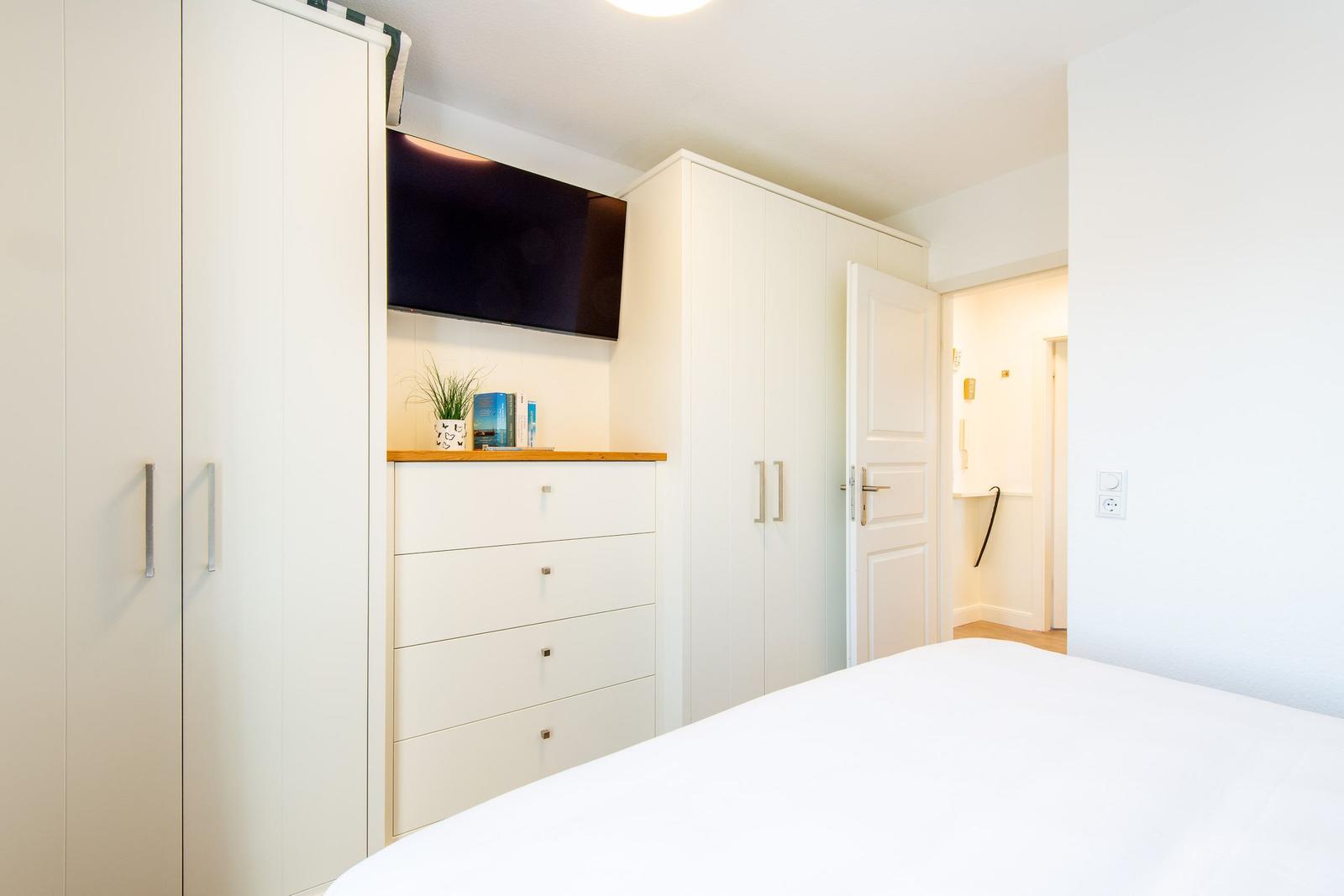 Schlafzimmer mit weißem Bett, Kleiderschränken und Fernseher an der Wand.