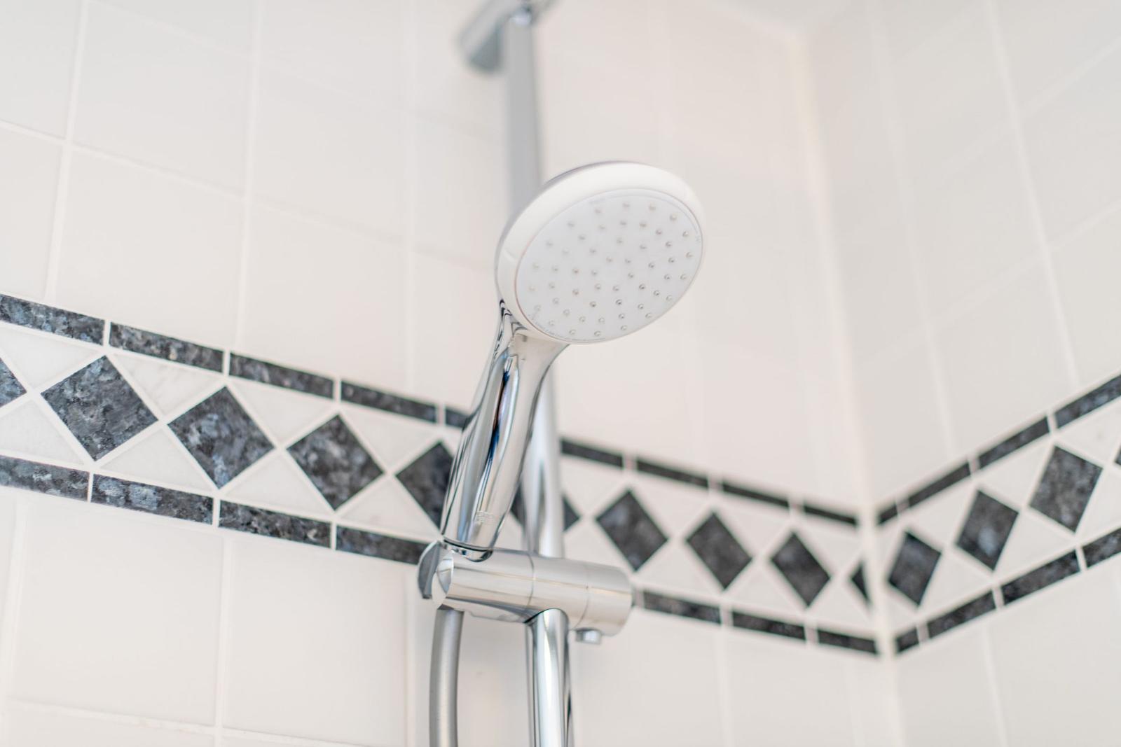 Duschbrause mit Chromarmatur und Mosaikfliesen an der Wand
