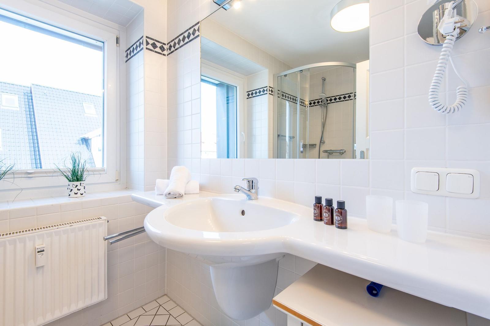 Badezimmer mit Waschbecken, Spiegel, Dusche und Fenster mit Pflanze.