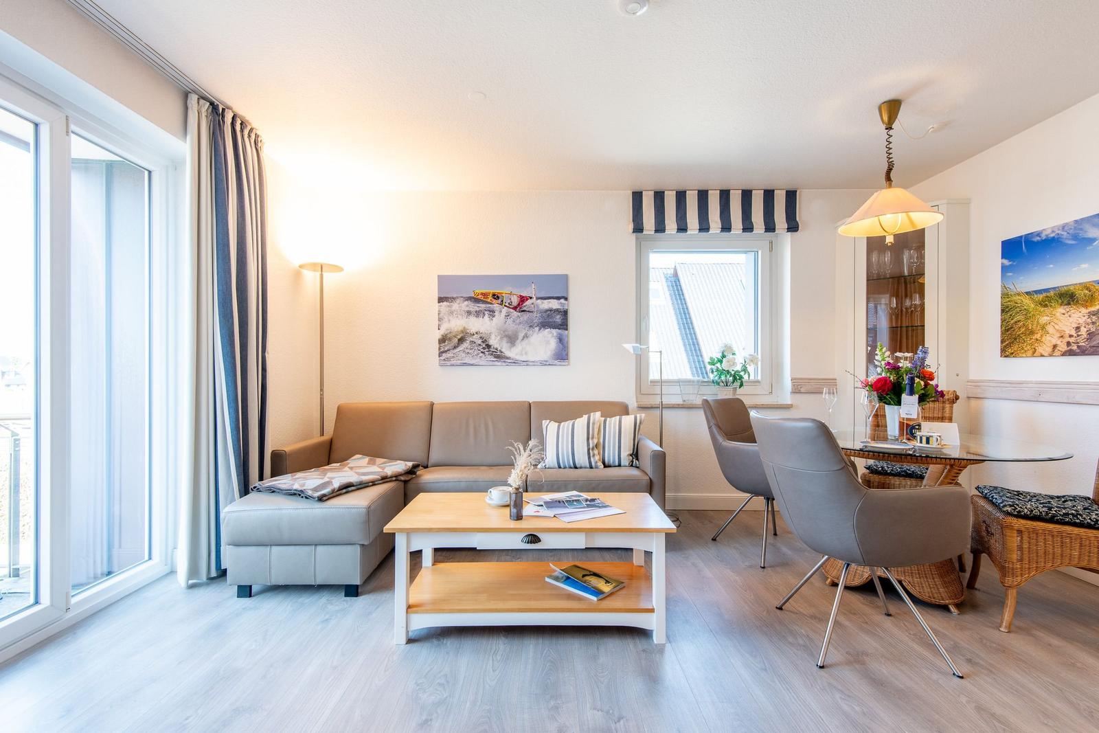 Wohn- und Essbereich mit Sofa, Tisch und Stühlen. Fenster und Bilder an den Wänden.