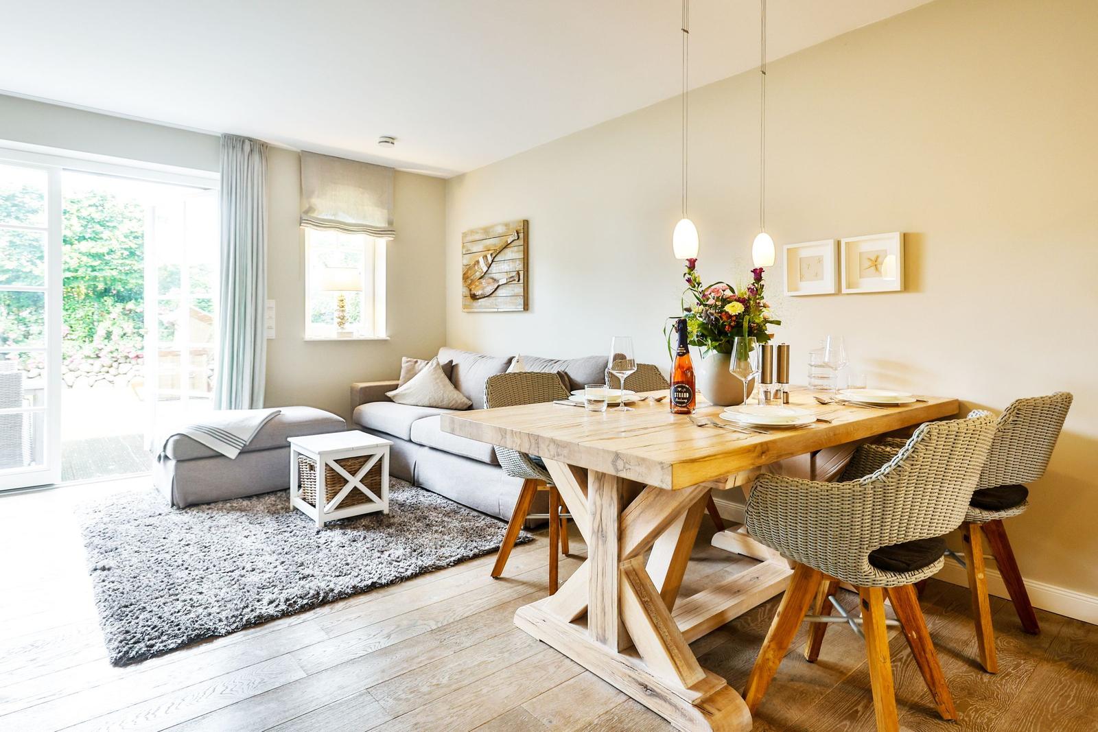 Dining area with wooden table and chairs. Living area with sofa and glass door. Wall decor and flowers.