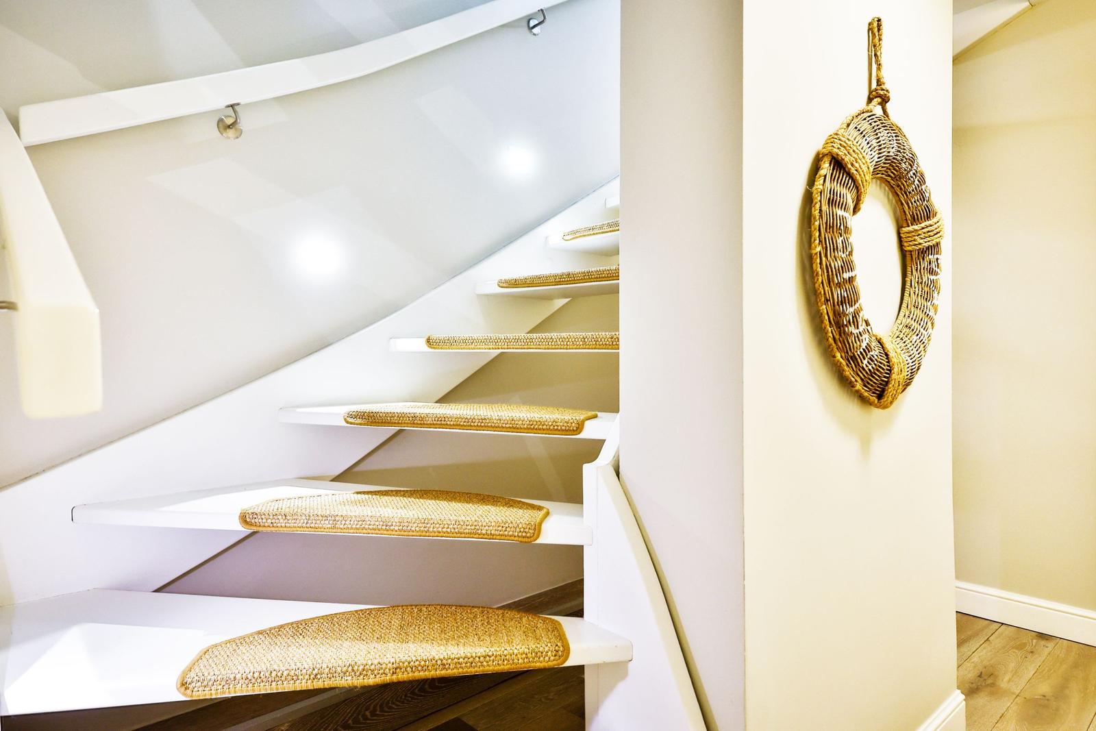 Staircase with white steps and straw-colored step mats. A woven ring hangs on the wall.