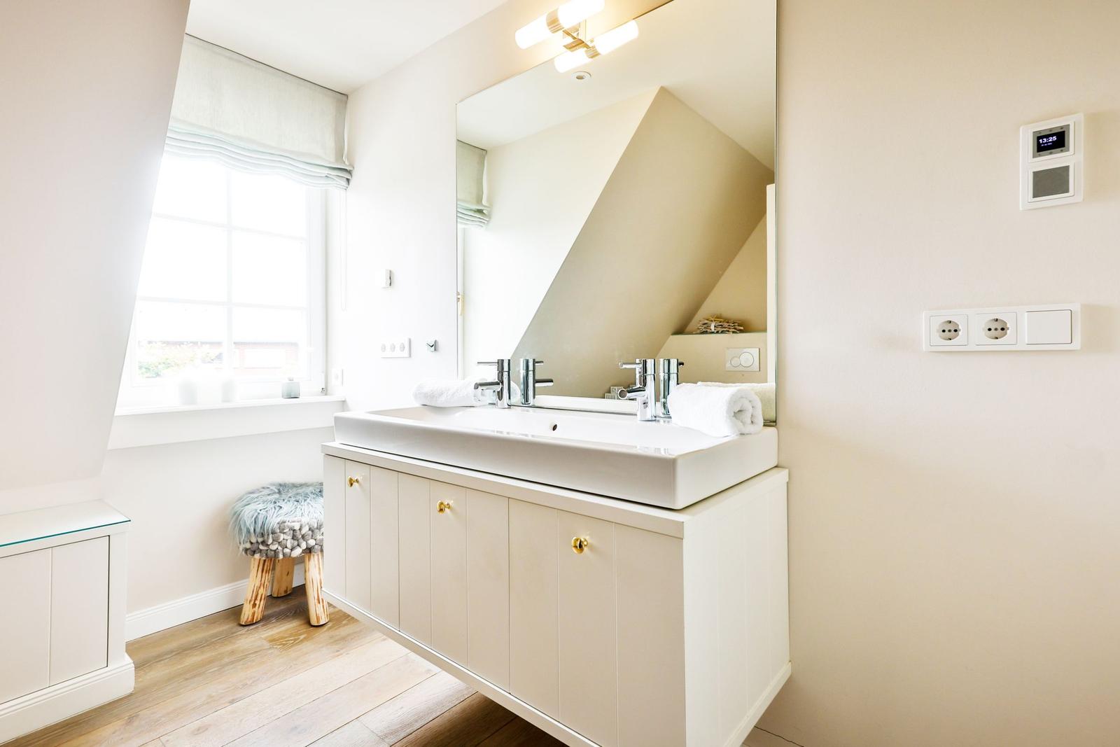 Bathroom with sink, mirror and window. Wooden floor and stool with fur cover.