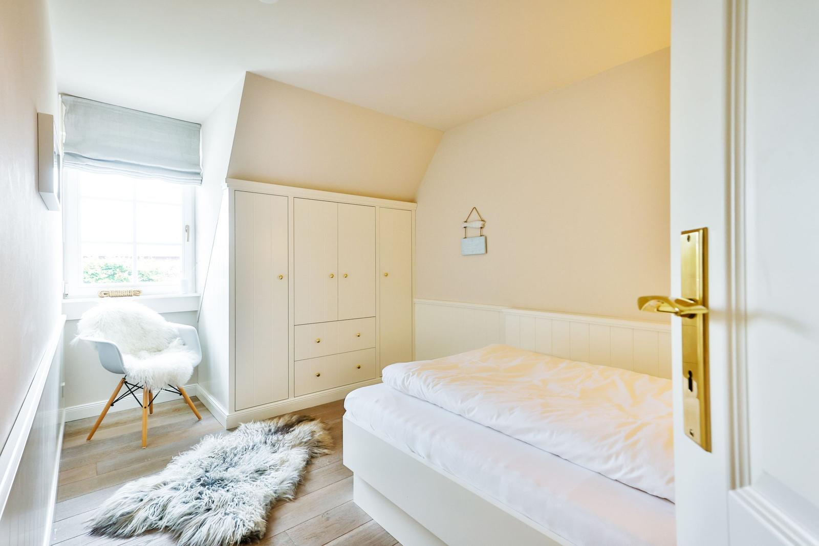 Bedroom with bed, wardrobe, and chair by the window.