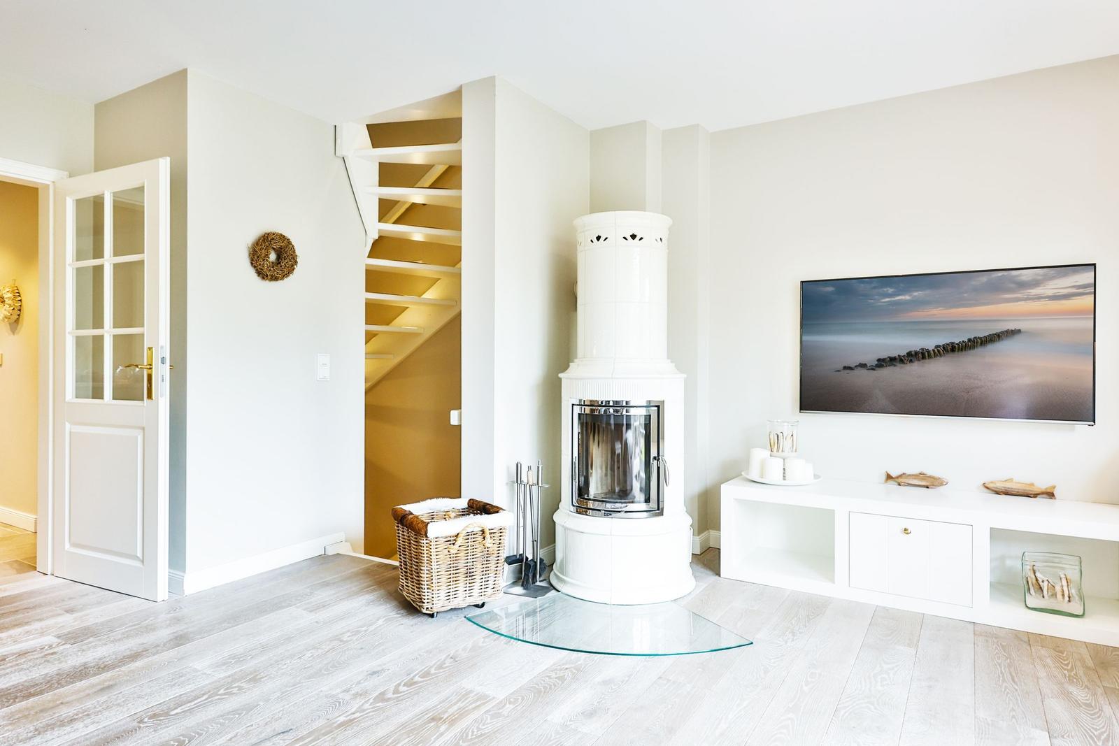 Living room with white fireplace, TV, and wooden floor. Stairs lead upstairs.