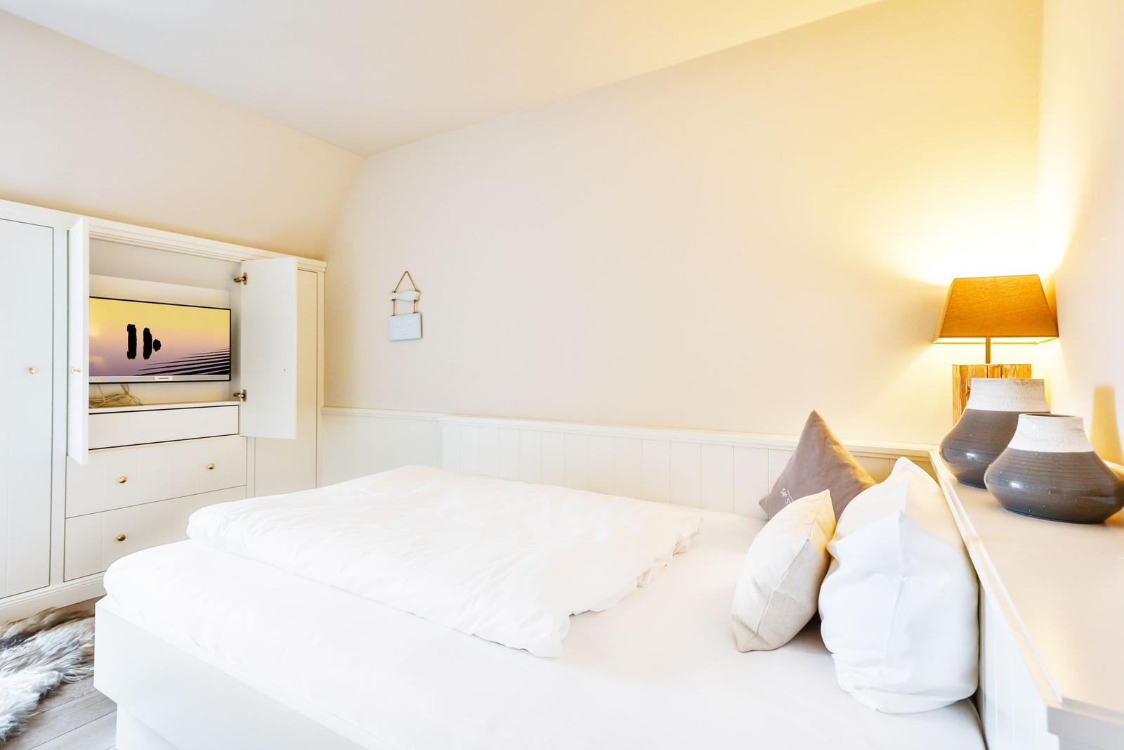 Bedroom with white bed, nightstand, lamp, and built-in TV.