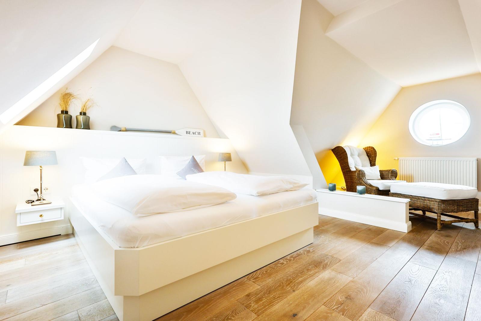 Bedroom with double bed, rattan chair, and round window.