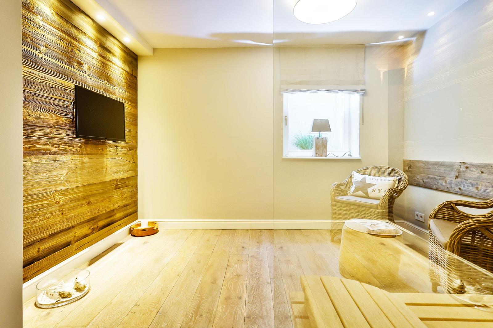 Room with wooden wall, TV, window and chair. Wooden floor and ceiling light.