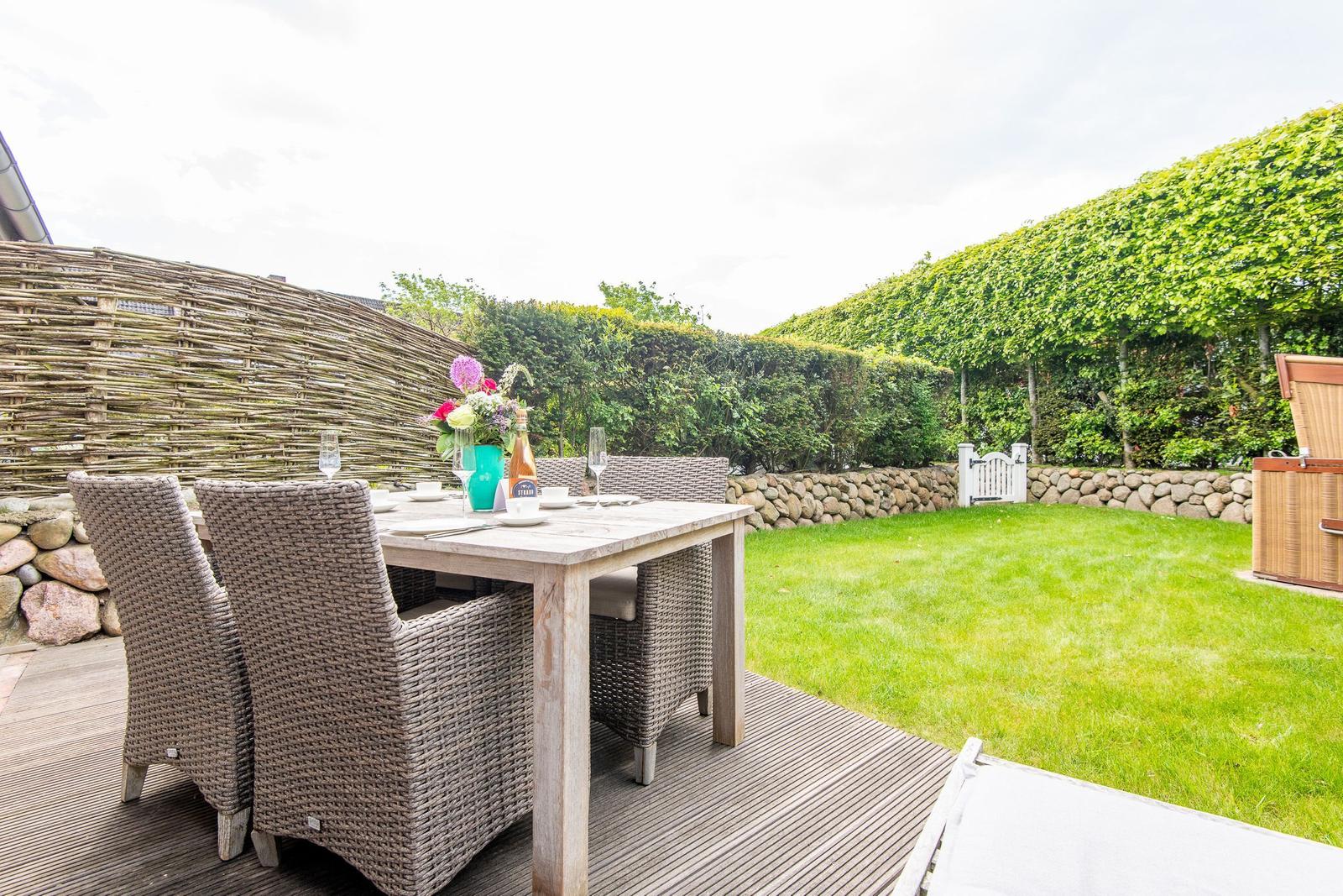 Rear yard with wooden deck, garden table, chairs, and green lawn.