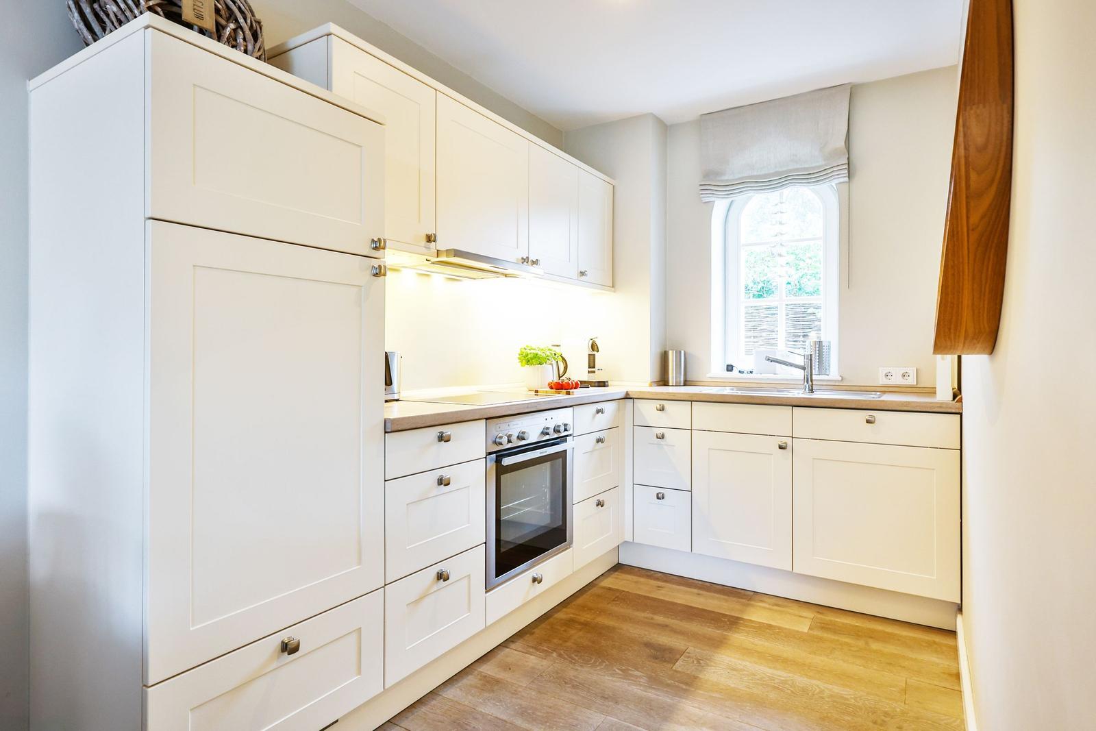 Kitchen with white cabinets, wooden floor, and window with roller blind.