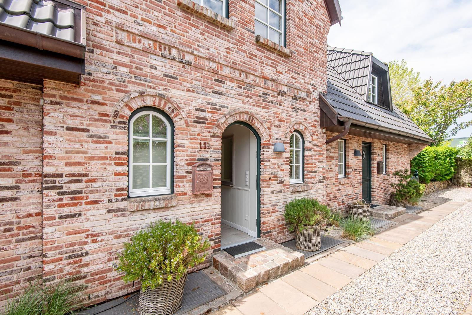 Two-story brick house with entrance door and windows. Plants in baskets near the entrance.