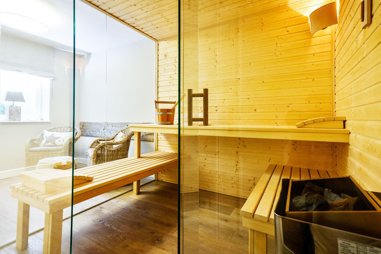 Sauna with wooden bench and glass wall. Chairs and a window are visible in the background.