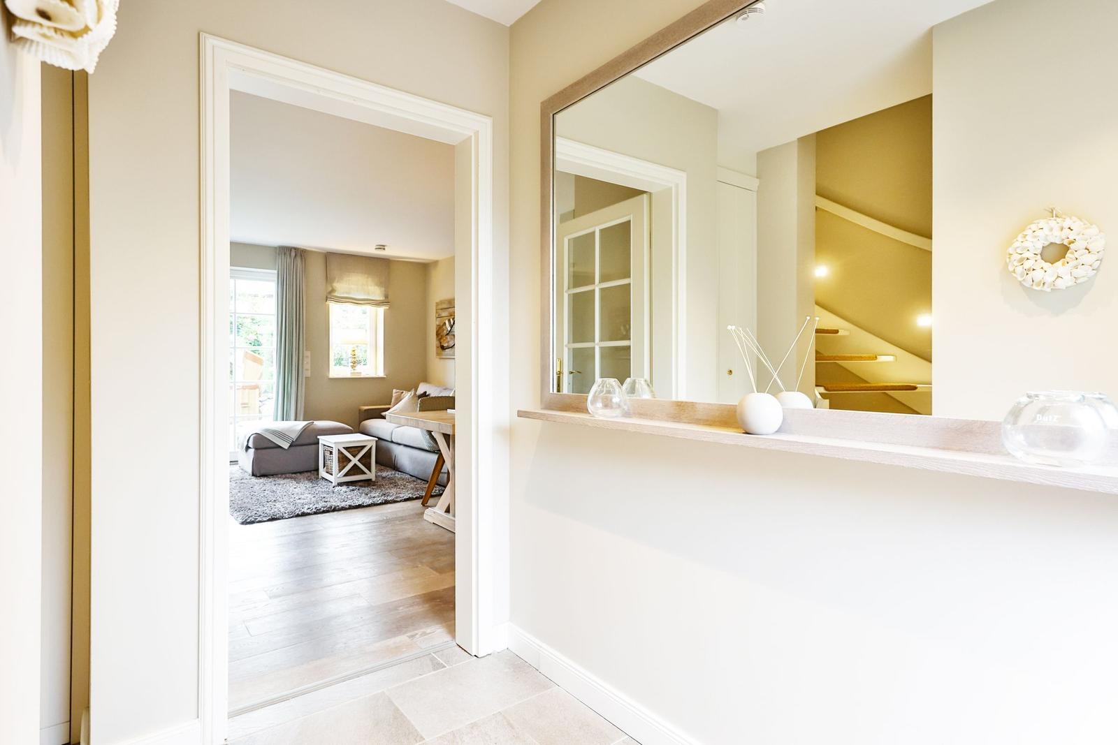 Hallway with mirror, tile floor, and view into living room with sofa and windows.