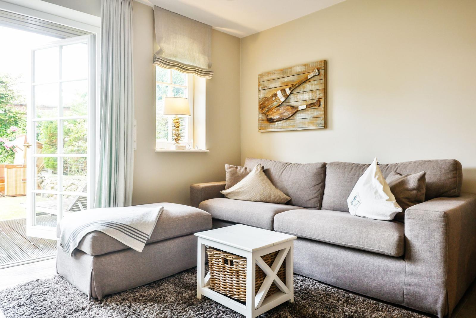 A living room with a gray sofa, ottoman, and white side table. A wooden decoration hangs on the wall.
