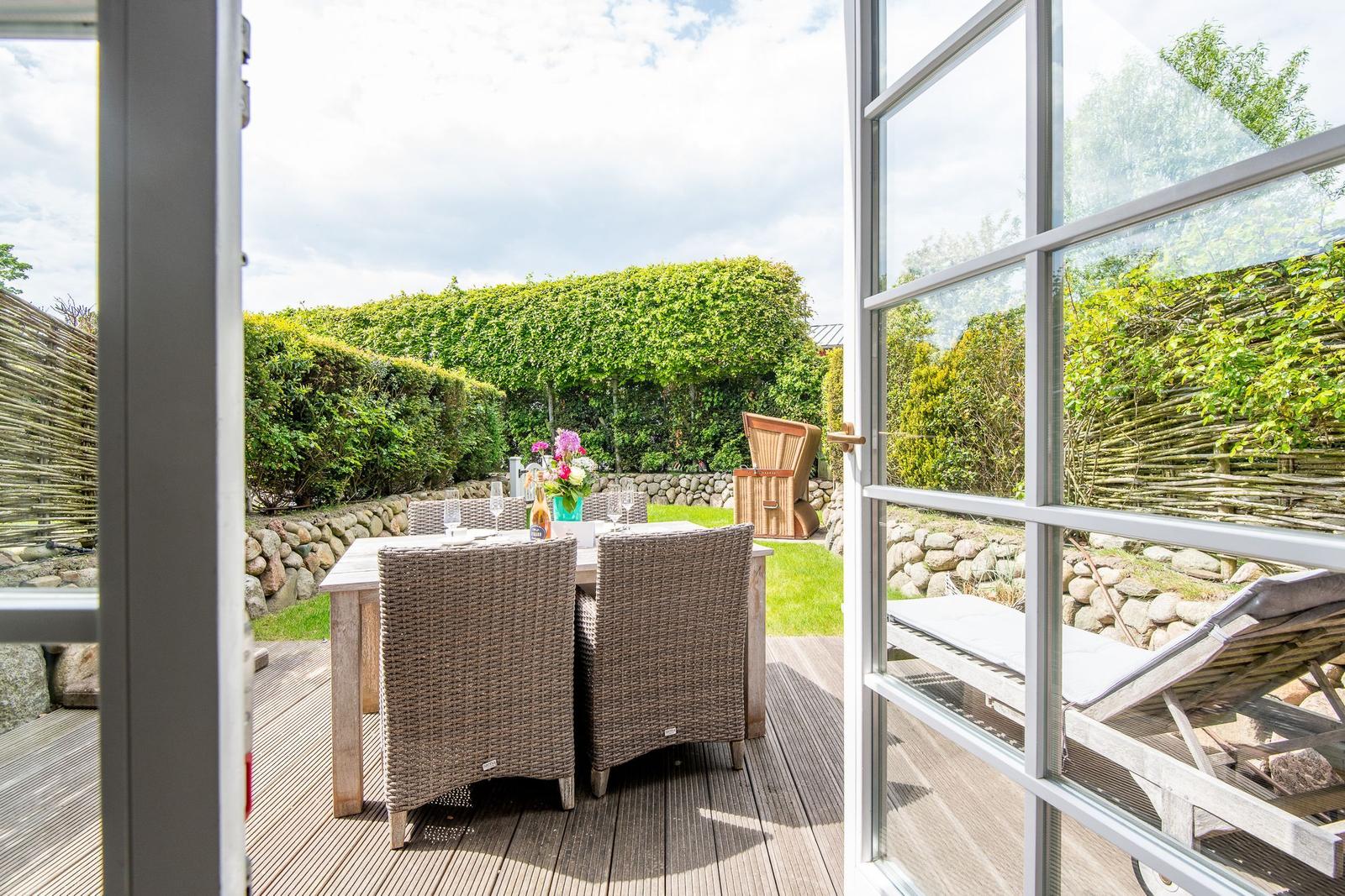 Deck with table, chairs, and lounge, surrounded by greenery and stone walls.