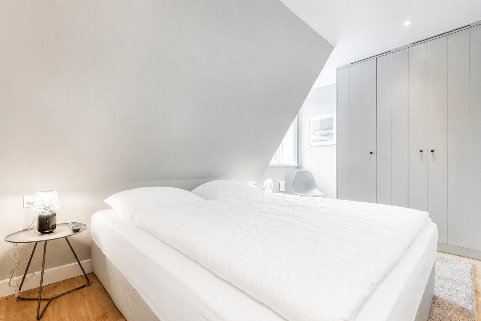 Schlafzimmer mit Doppelbett, Kleiderschrank und Nachttisch unter schräger Decke.