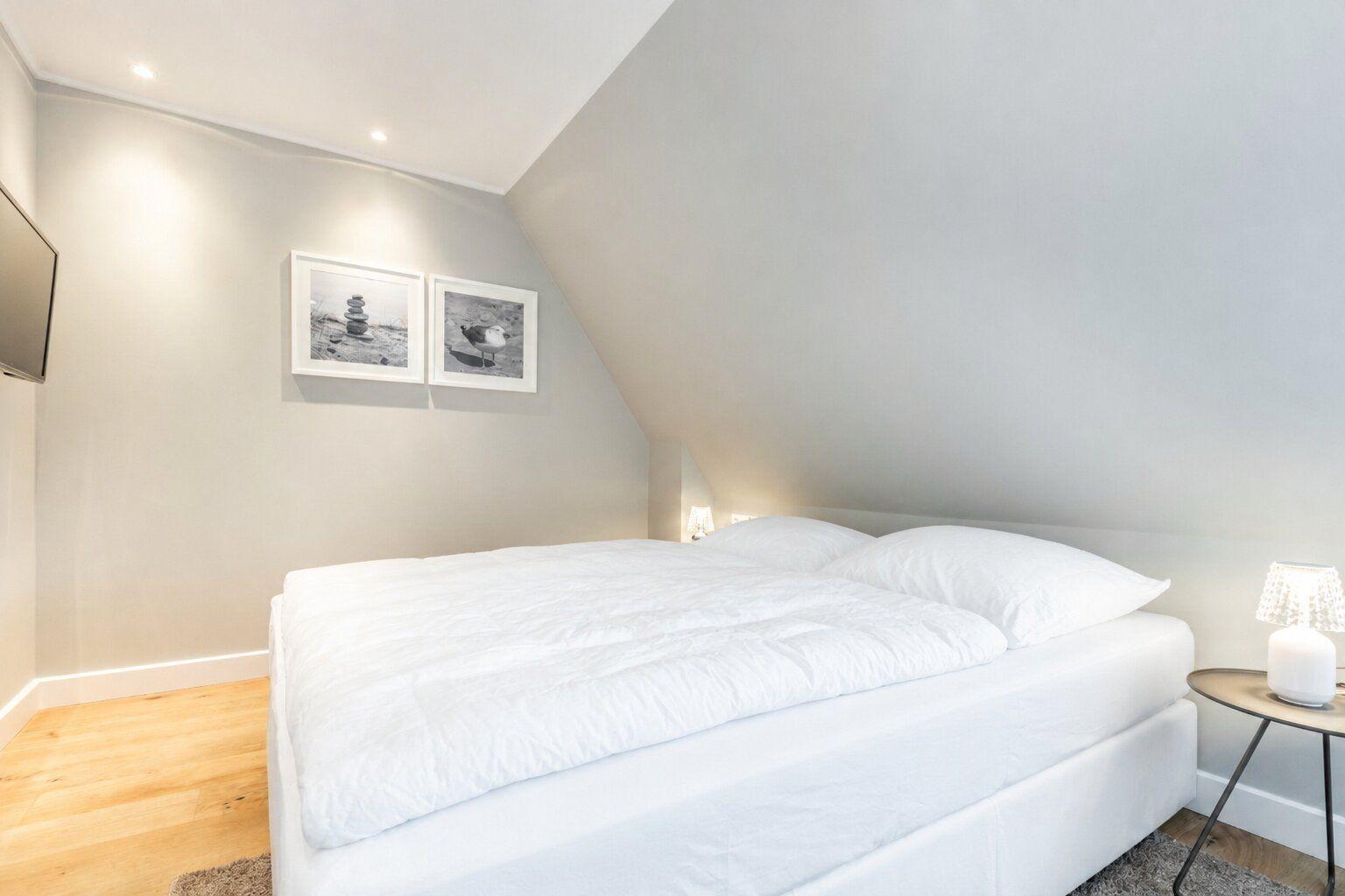 Schlafzimmer mit Doppelbett, Holzboden und schrägen Wänden. An der Wand hängen zwei Bilder.