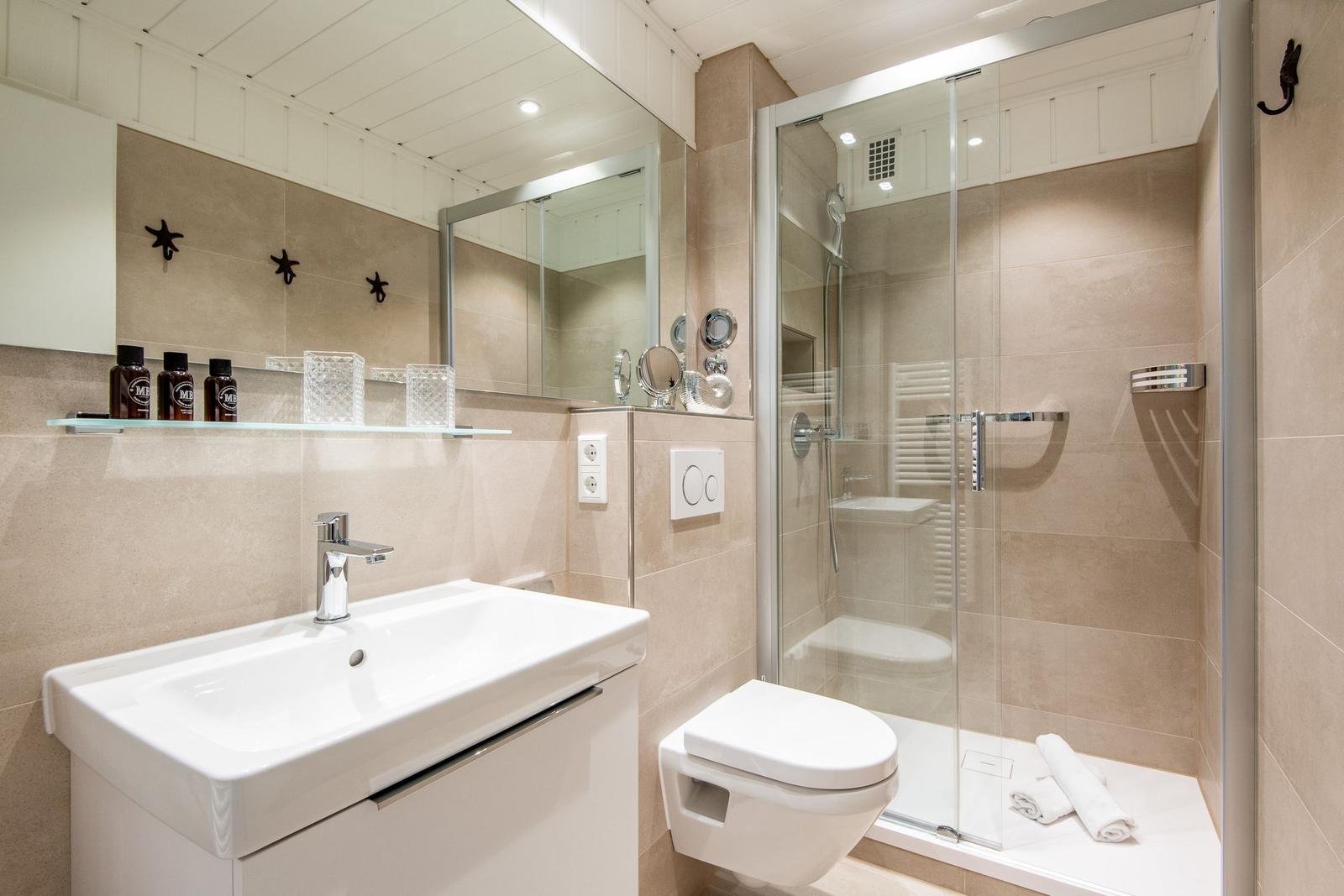 Badezimmer mit Dusche, Waschbecken und Toilette. Wandfliesen und Spiegel sichtbar.
