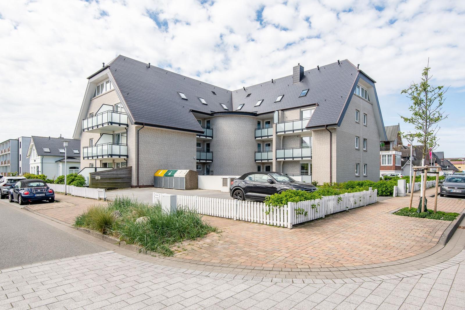 Modern multi-family house with balconies and paved forecourt.