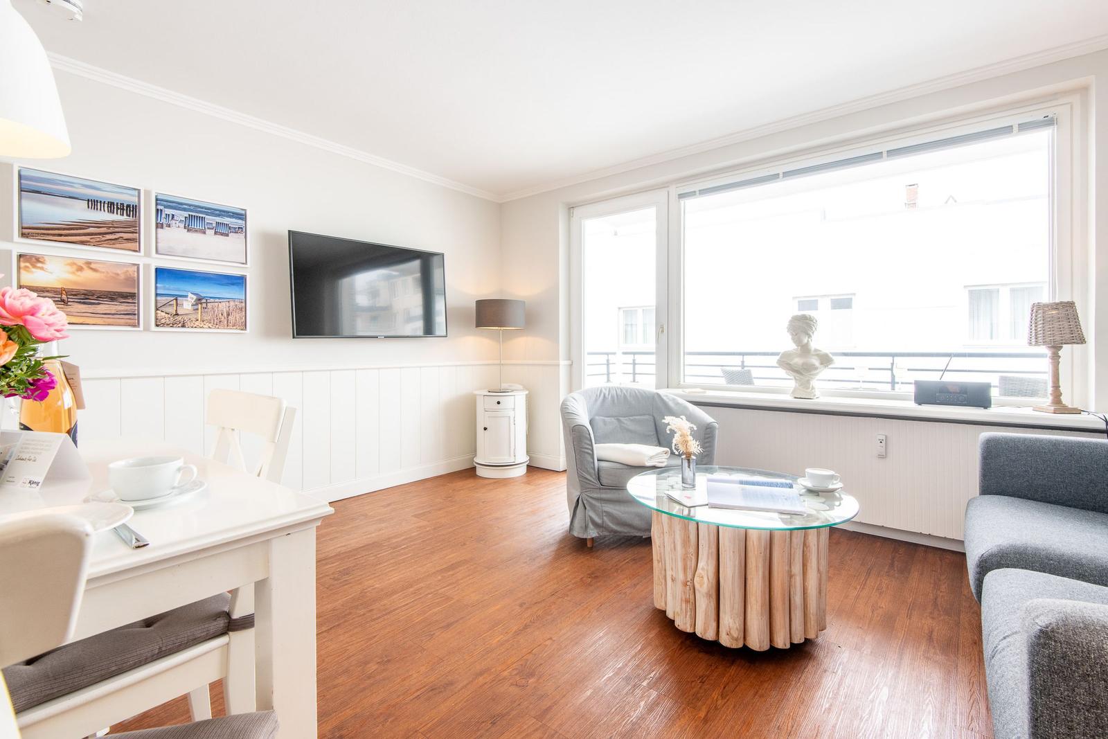 Wohnzimmer mit TV, Glas-Tisch, Sessel und Fenster zum Balkon.
