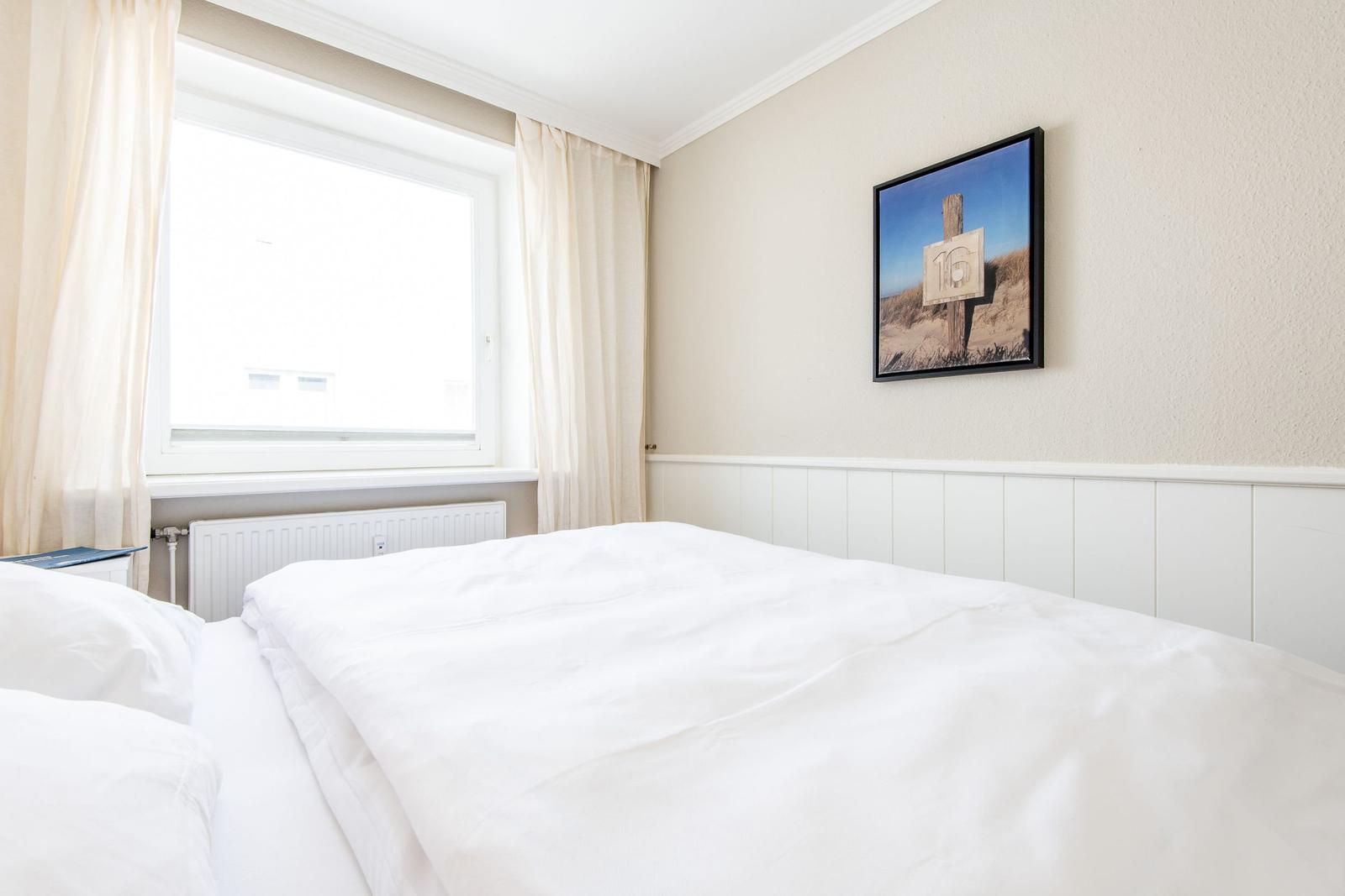 Schlafzimmer mit weißem Bett, Fenster und Wandbild mit Zahlen.