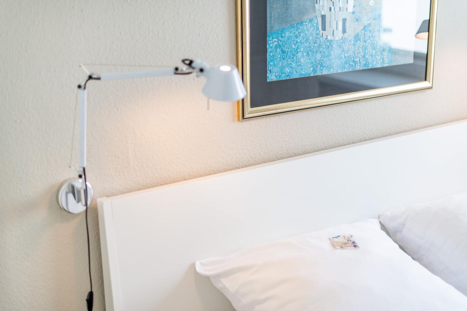 Hochwertige Wandlampe neben weißem Bett und Bild an der Wand.