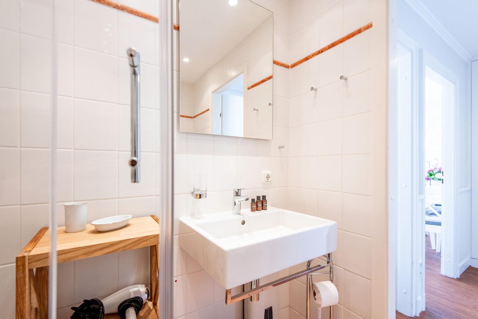 Badezimmer mit Waschbecken, Spiegel und Dusche mit Holzregal.