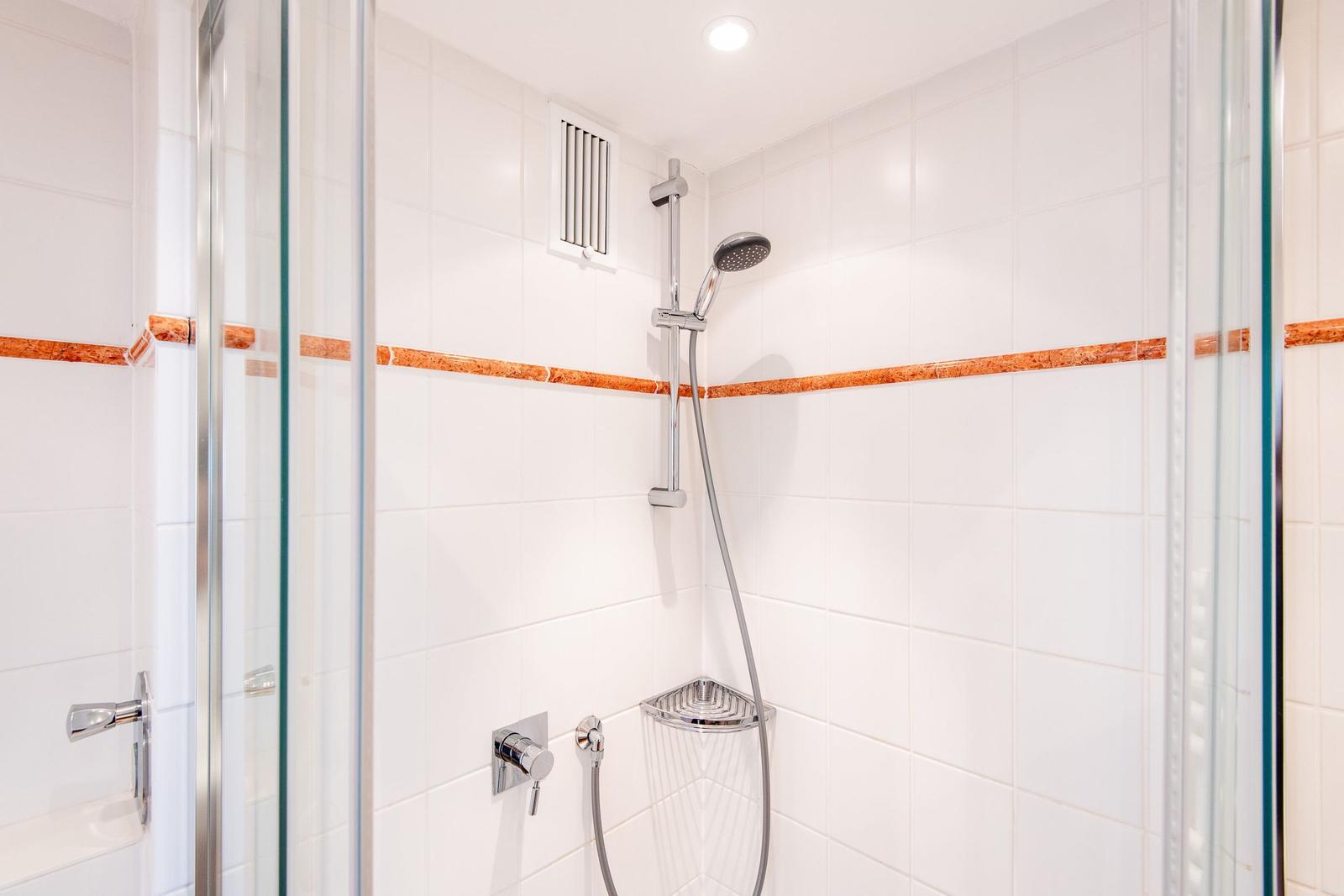 Dusche mit Glaswand, weißen Fliesen und orangefarbener Zierleiste.