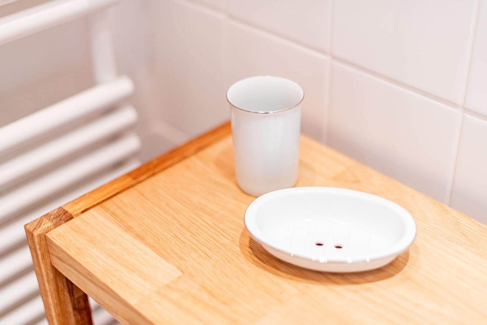 Holztisch mit weißem Becher und Seifenschaumbecher in Badezimmer.