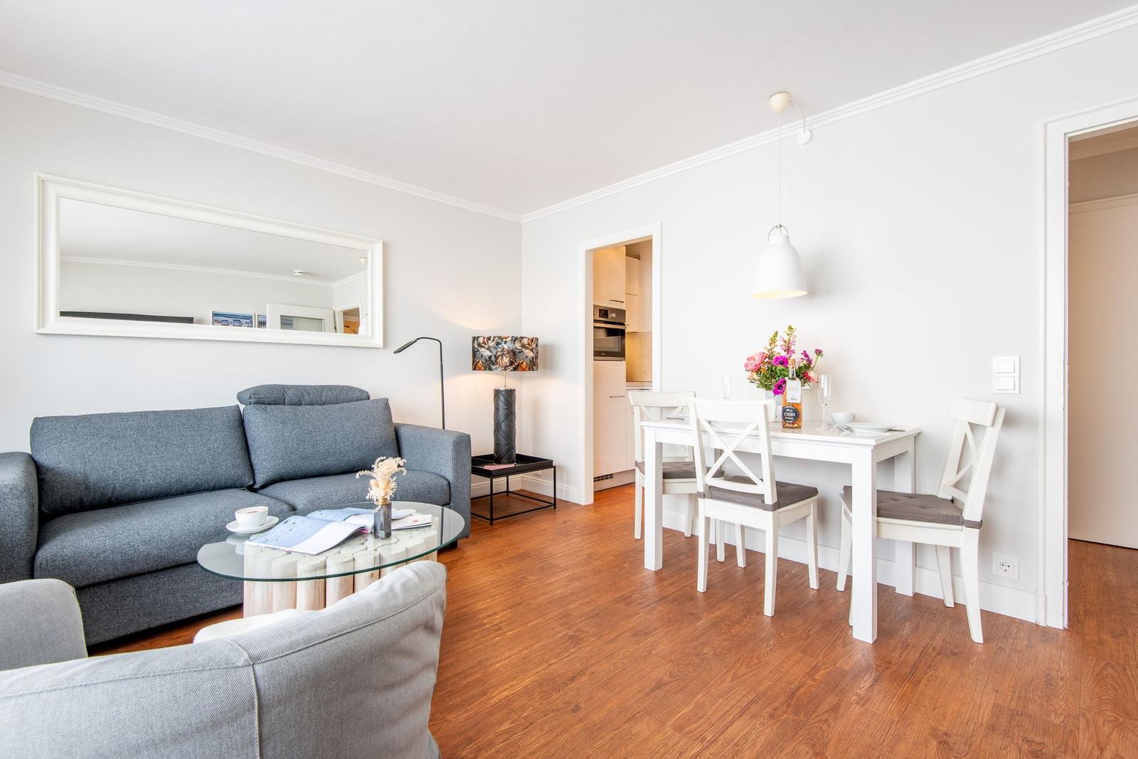 Wohn- und Essbereich mit grauem Sofa, weißem Tisch und Stühlen sowie Holzboden.