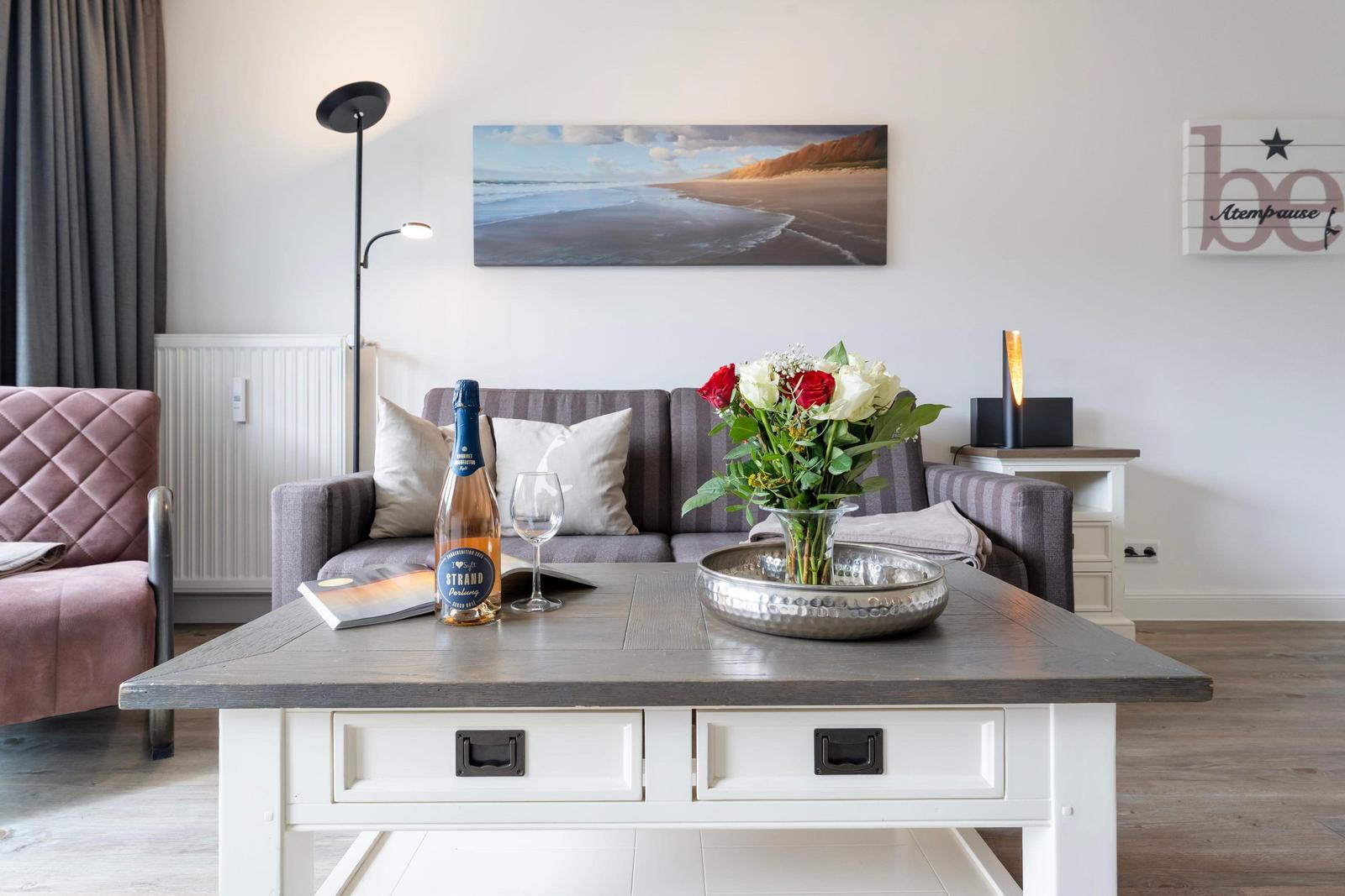 Living room with sofa, coffee table, and flower arrangement. Wall picture shows beach.