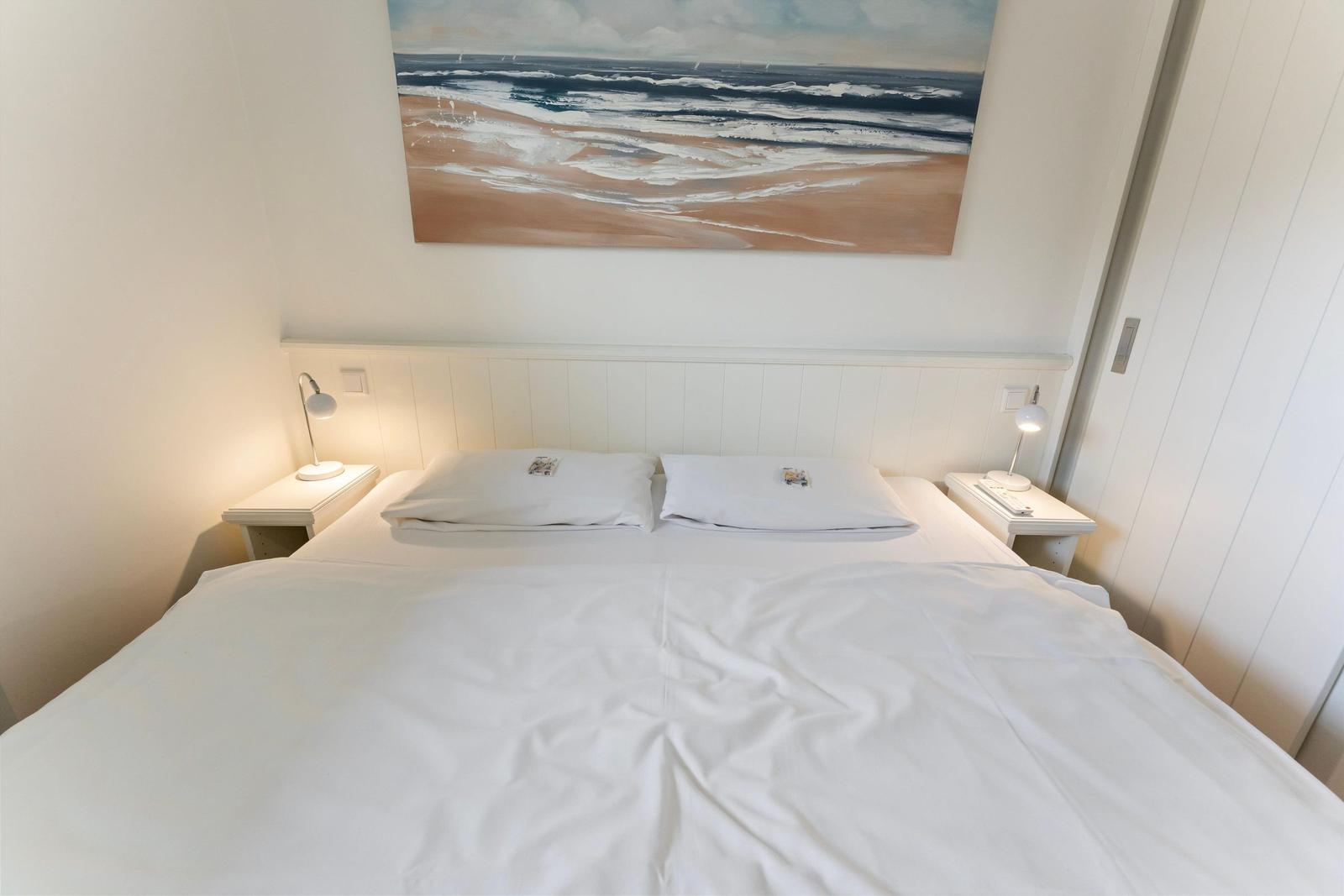 Bedroom with double bed, two nightstands, and wall art with beach motif.