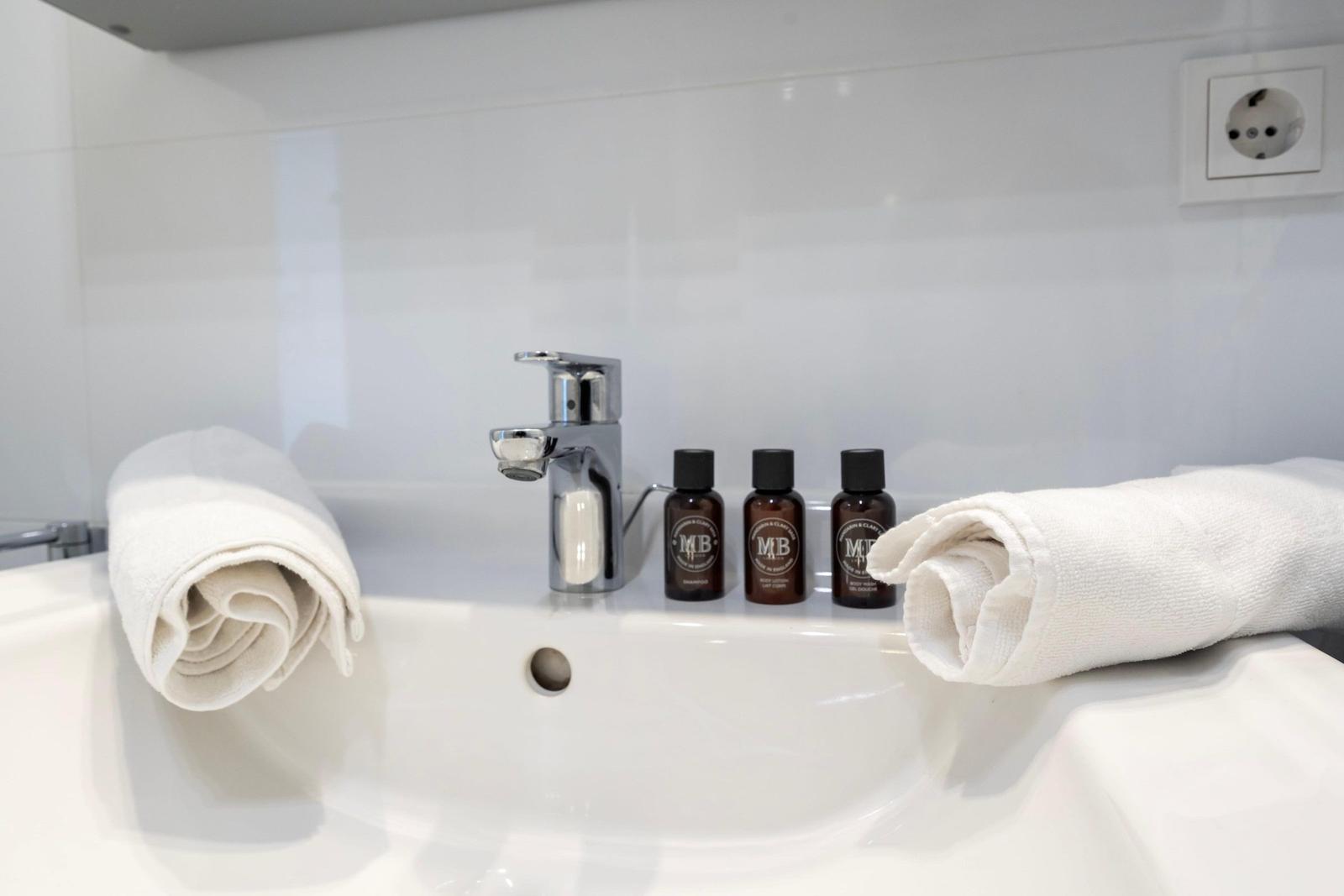 Sink with faucet, three bottles, and two rolled towels.