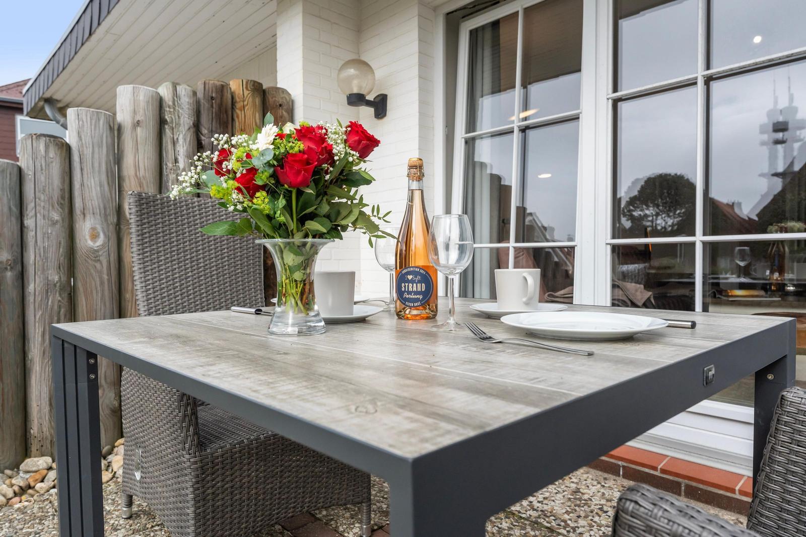Outdoor table with flowers, wine bottle, and dishes in front of house with windows.
