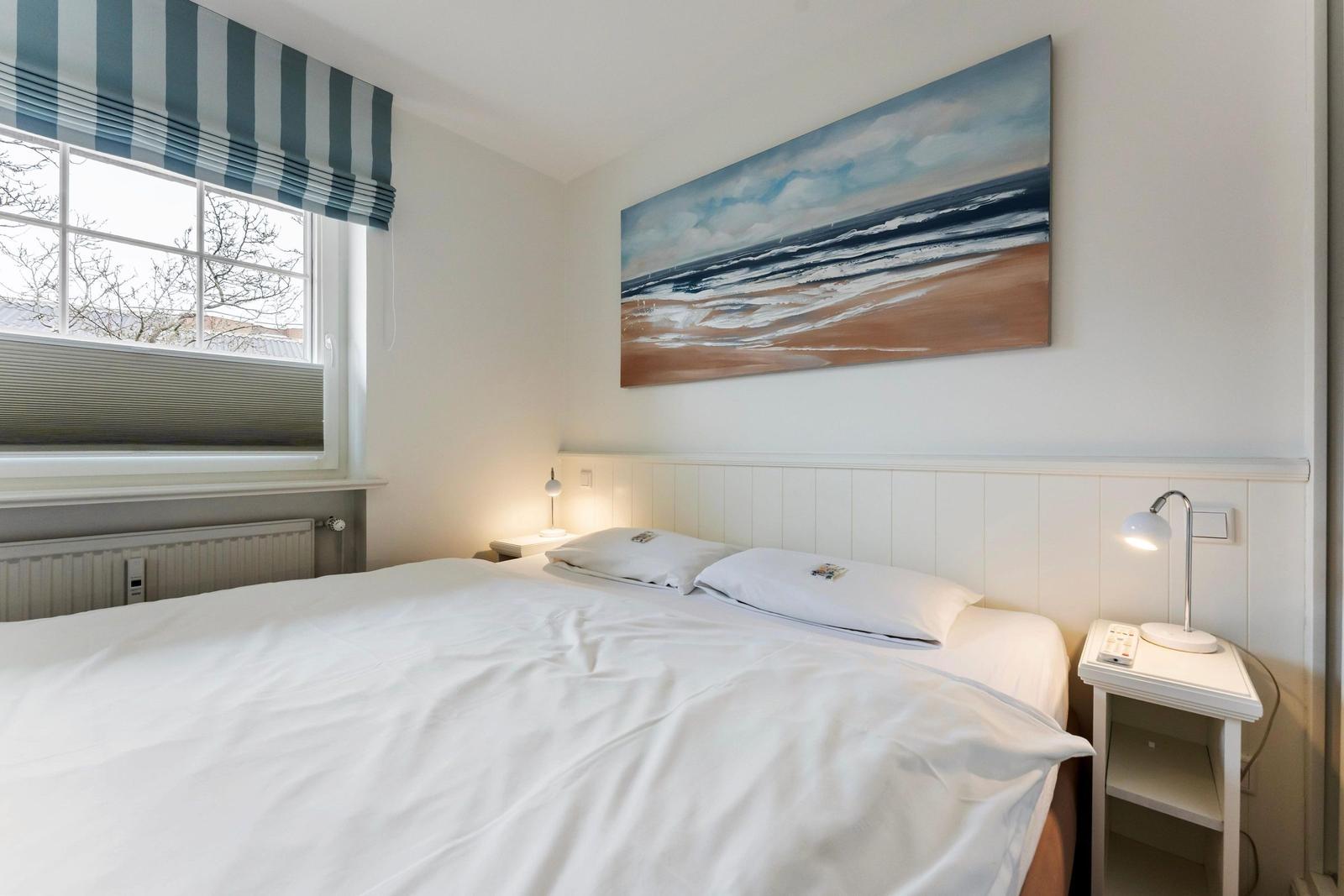 Bedroom with bed, nightstand, and wall art. Window with blinds and awning.