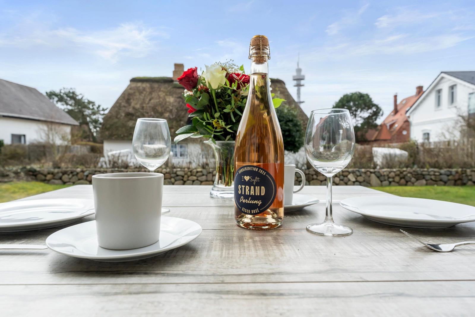 Table with bottle, glasses, and flowers outdoors