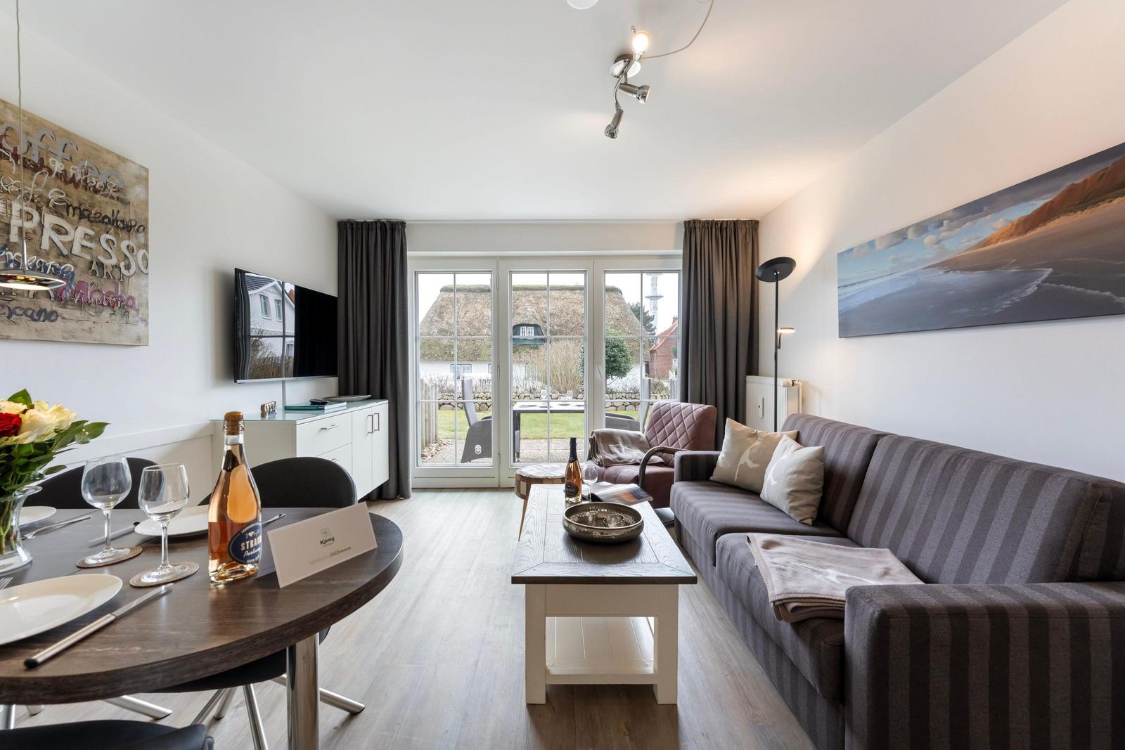 Living and dining area with sofa, table, and view of the garden.