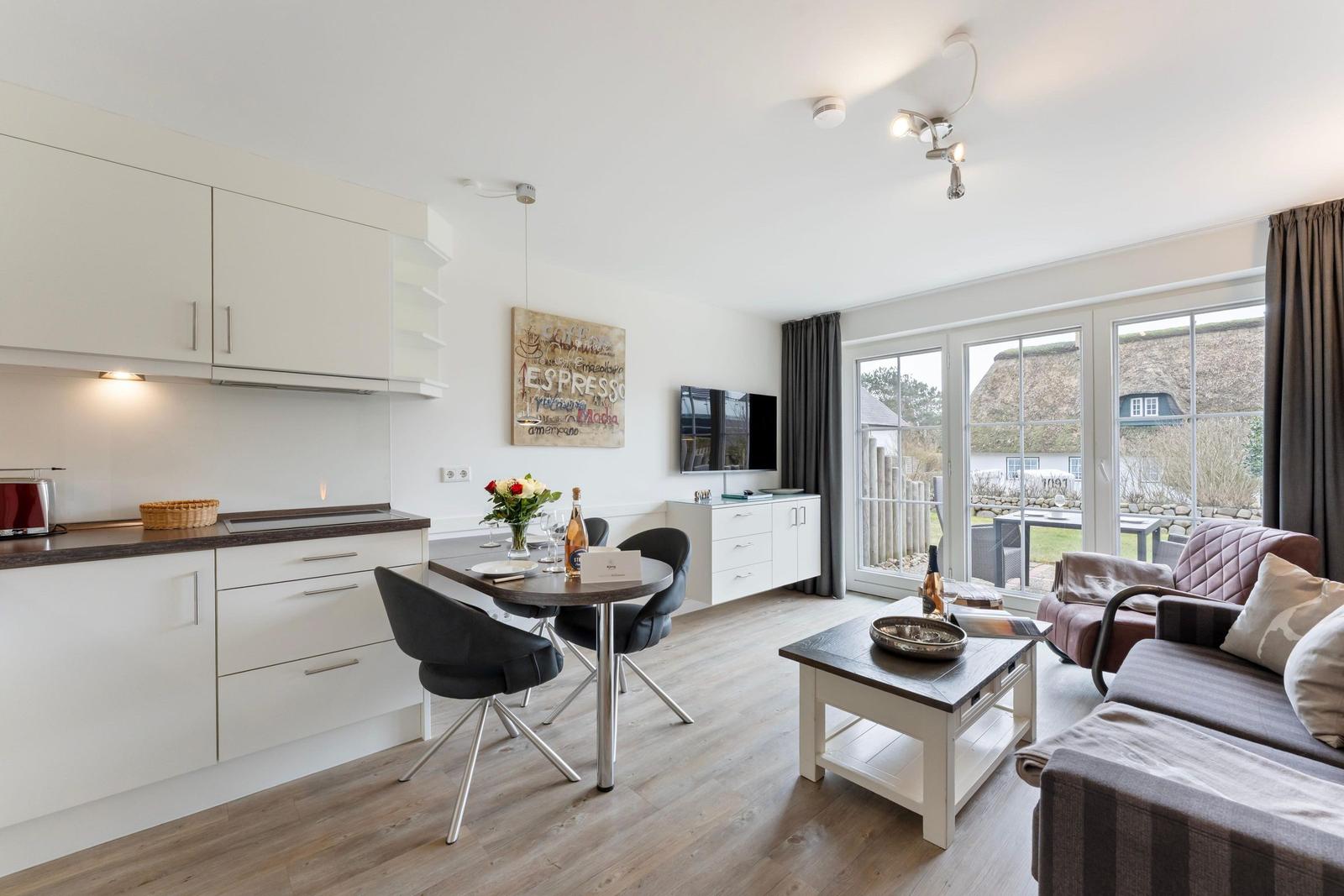Living kitchen with dining table, sofa, and TV. Doorway to terrace with view of thatched roofs.