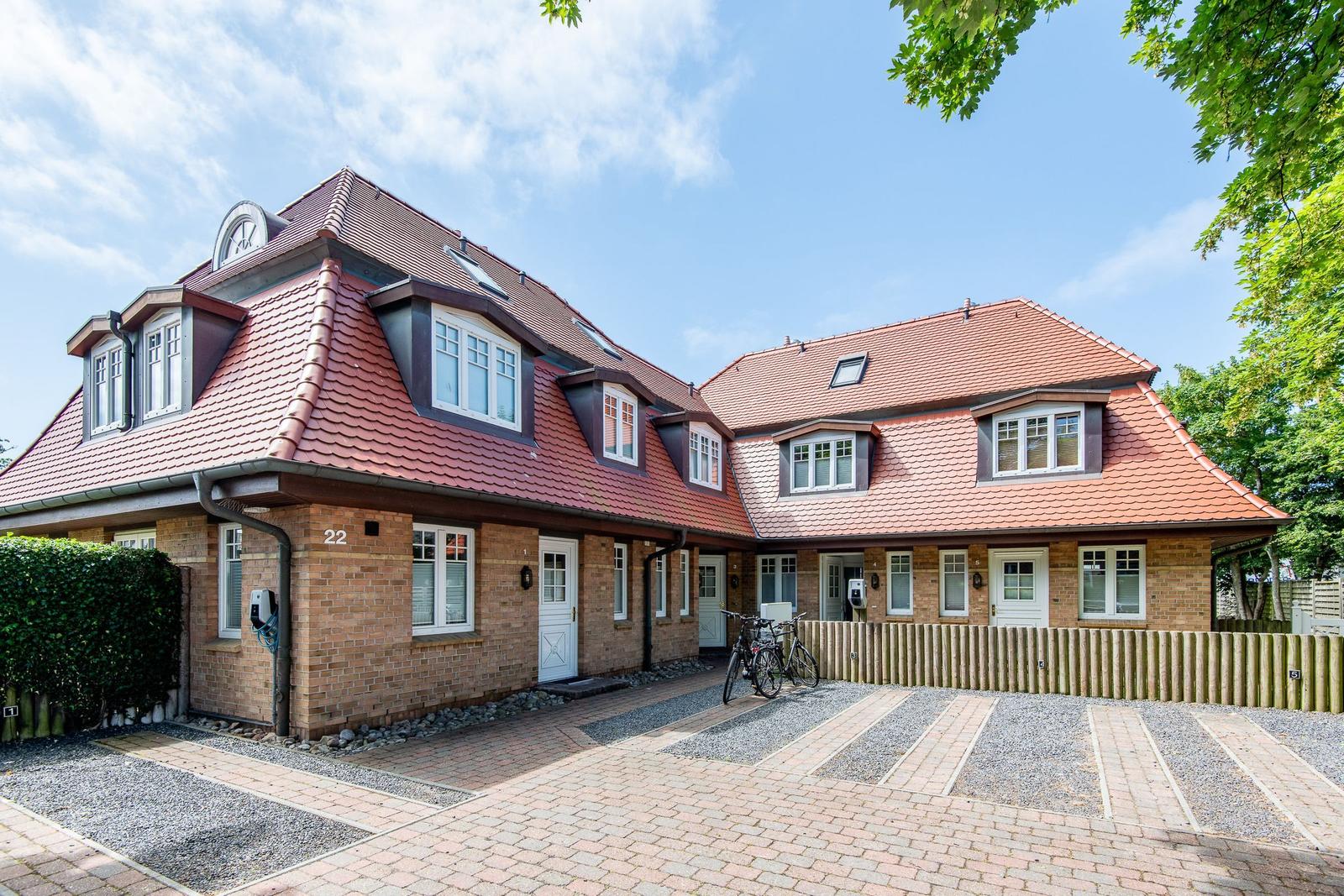 Haus mit rotem Dach, Backsteinfassade und mehreren Fenstern. Vorgarten mit Fahrrädern und Holzzaun.